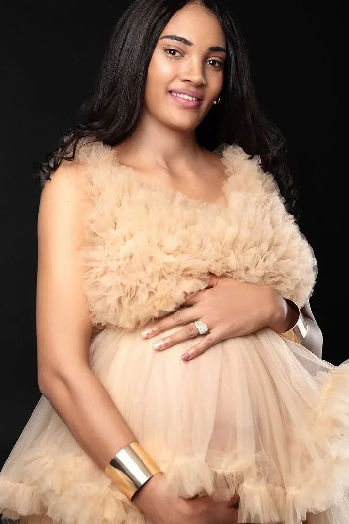 A pregnant woman wearing a beige coloured puffy tulle maternity gown in studio photoshoot
