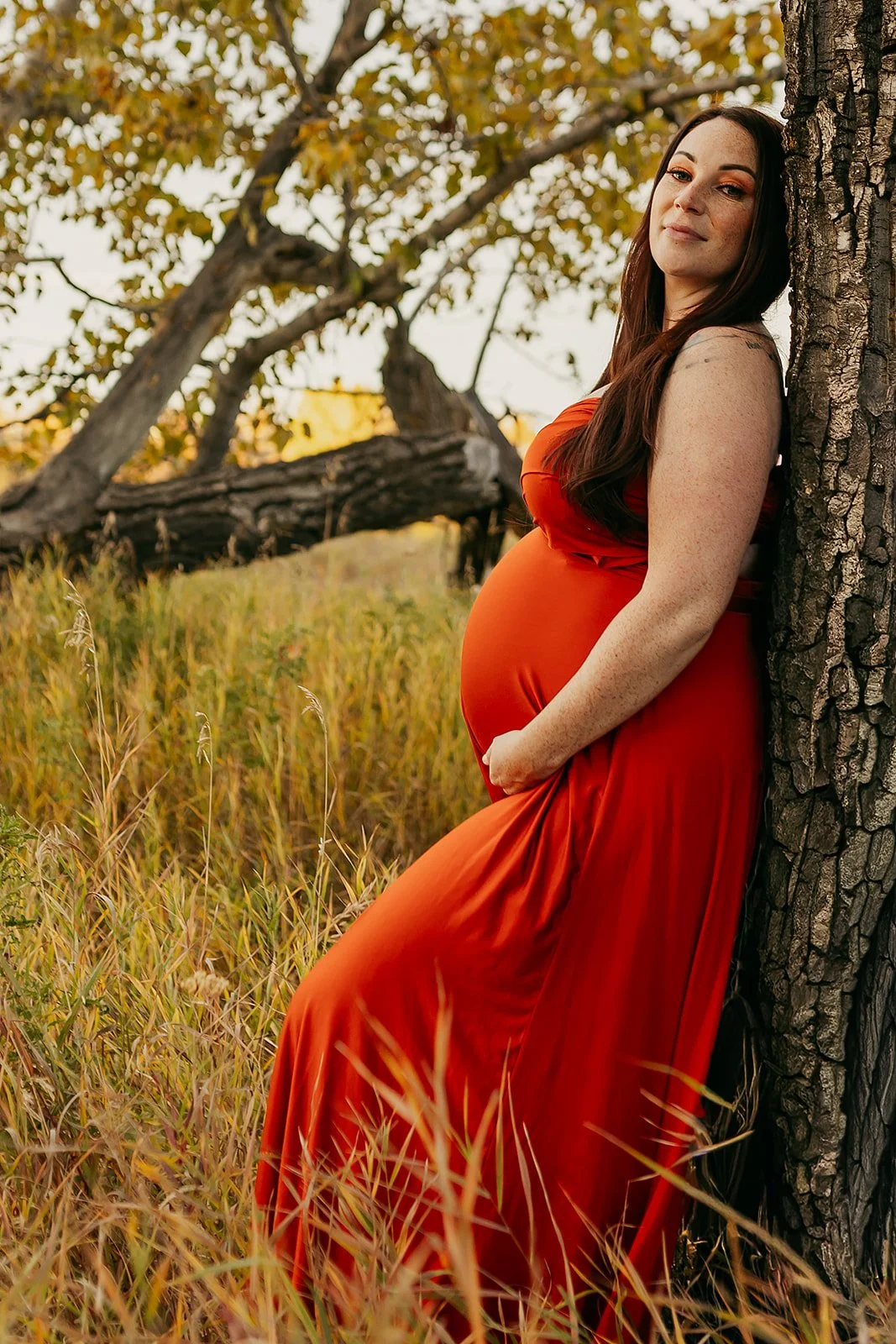 A pregnant woman wearing an orange red maternity infinity wrap dress in an autumn field outdoor photosession