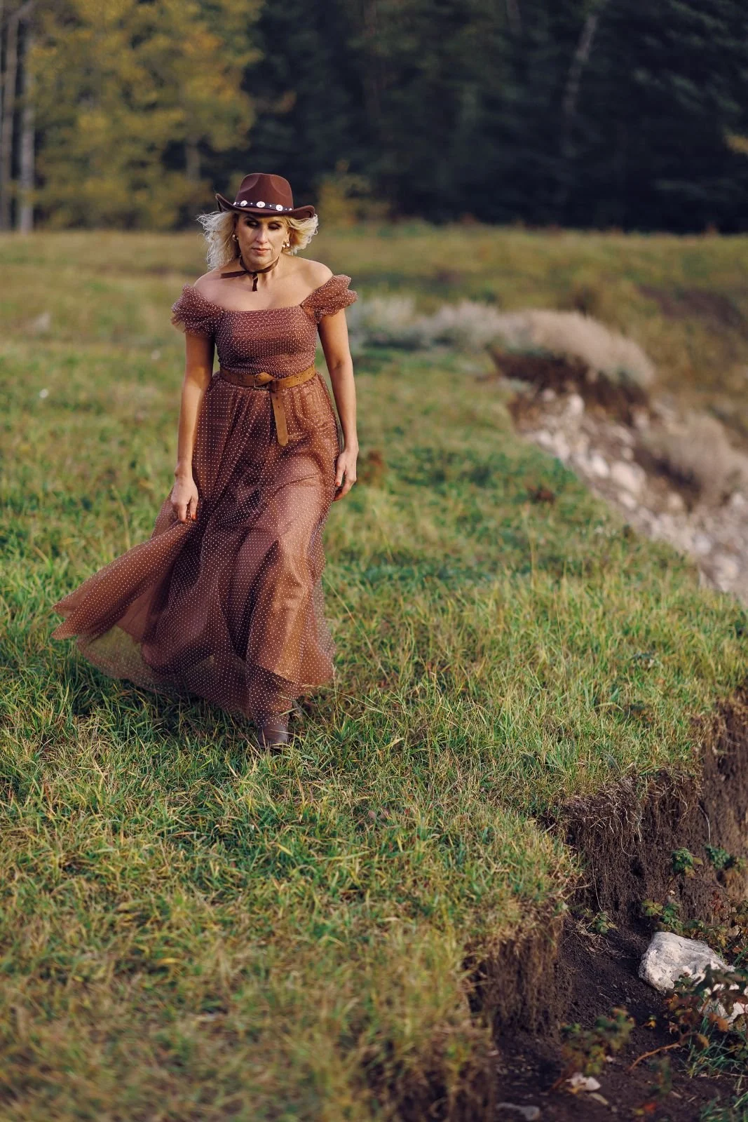 A woman wearing a rust brown tulle gown with white polkadots with a cowboy hat