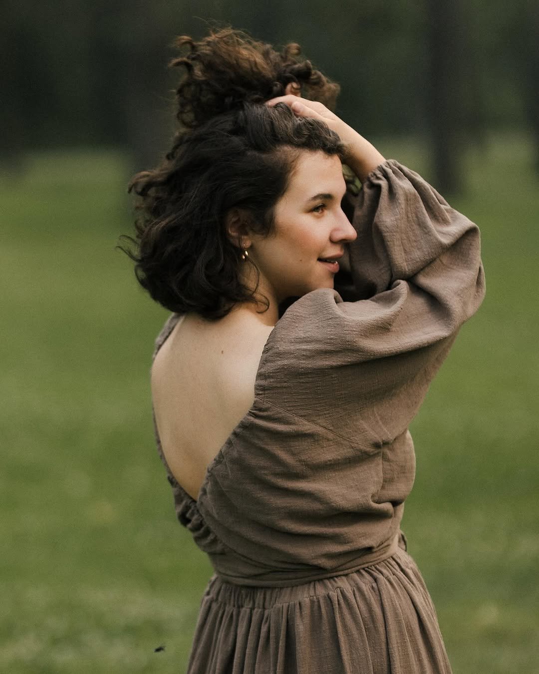 A woman holding her hair, wearing an open back khaki brown dress in an outdoor photoshoot in Calgary