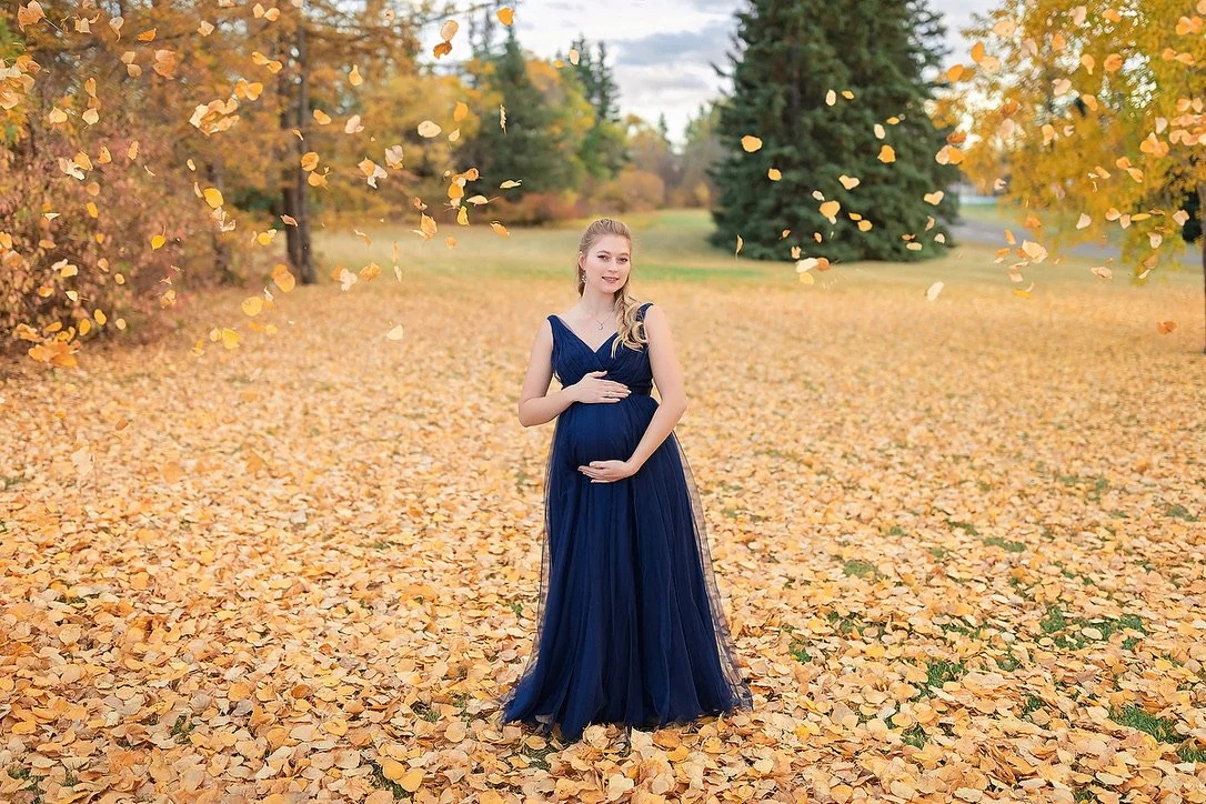 A pregnant woman in outdoor fall photoshoot wearing a navy blue tulle rental gown