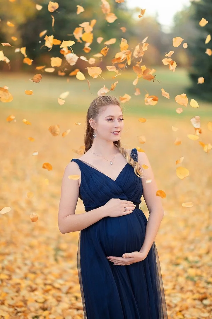 A pregnant woman in outdoor fall photoshoot wearing a navy blue tulle rental gown