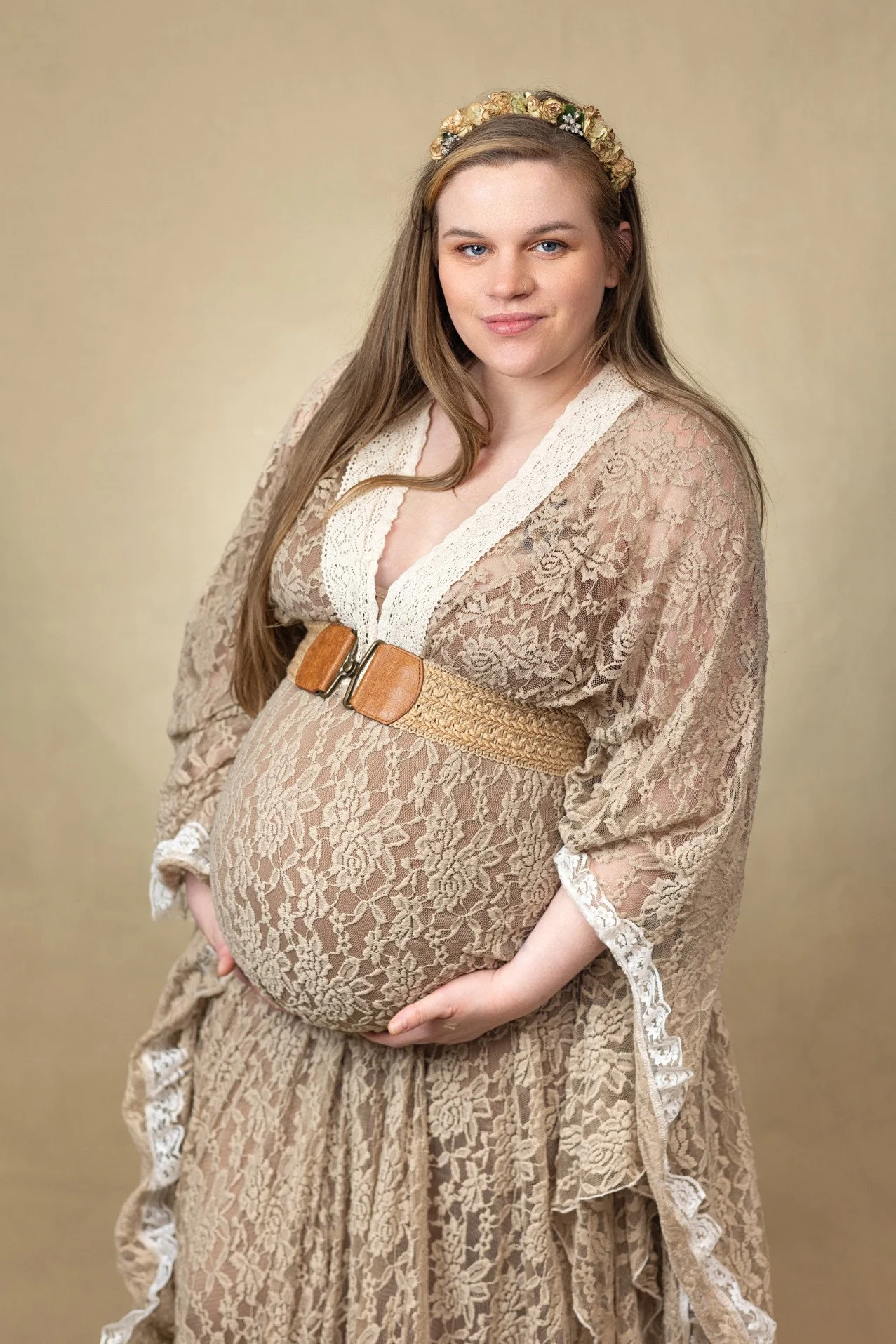 Close up of a pregnant woman, showing her wearing a lace khaki-coloured dress in an indoor photoshoot setting