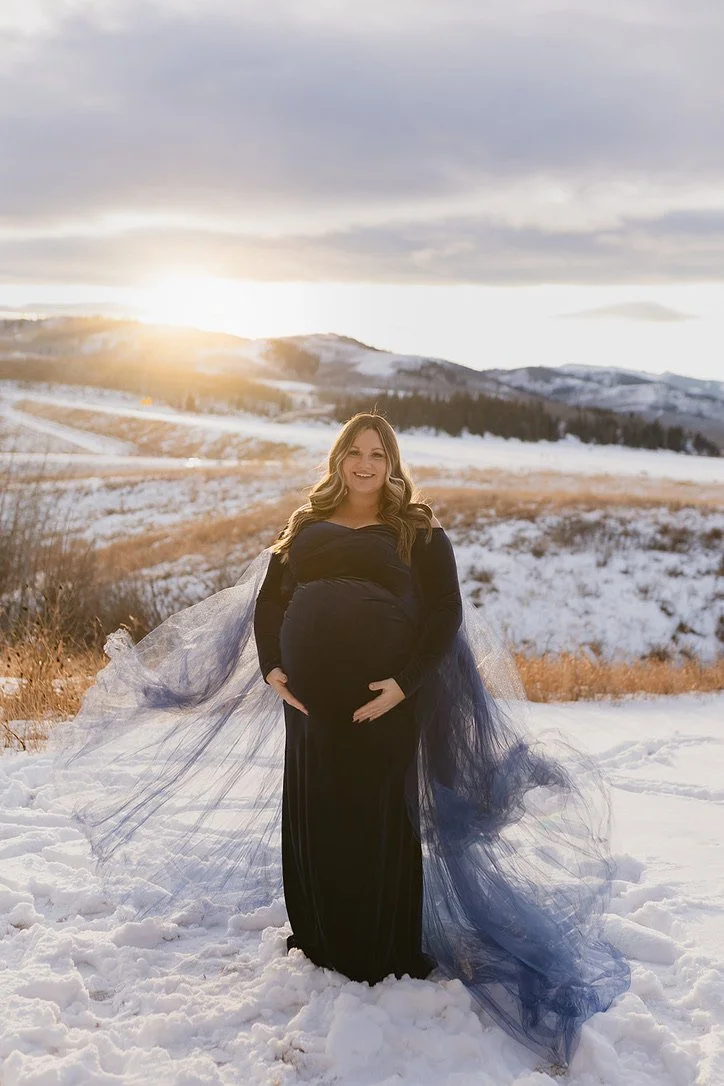 A pregnant woman wearing a navy dress and blue tulle overskirt in outdoor Calgary maternity photoshoot