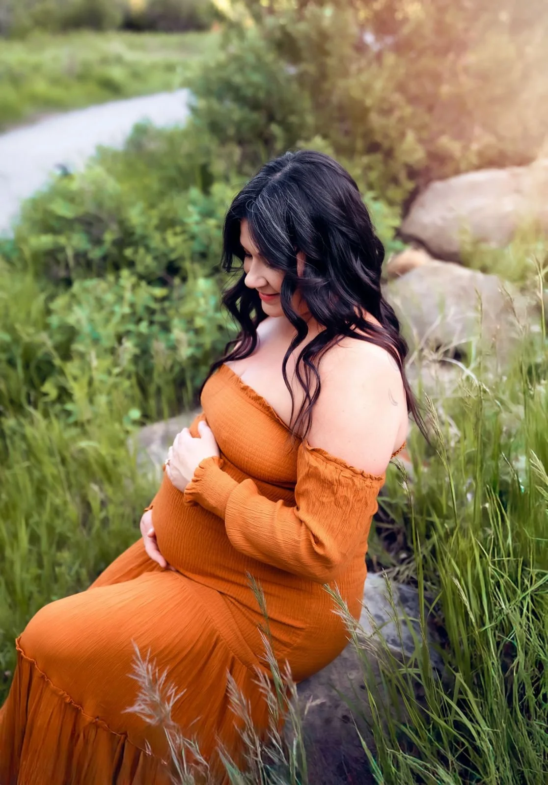 A pregnant woman in a strapless orange boho mermaid dress, sitting down