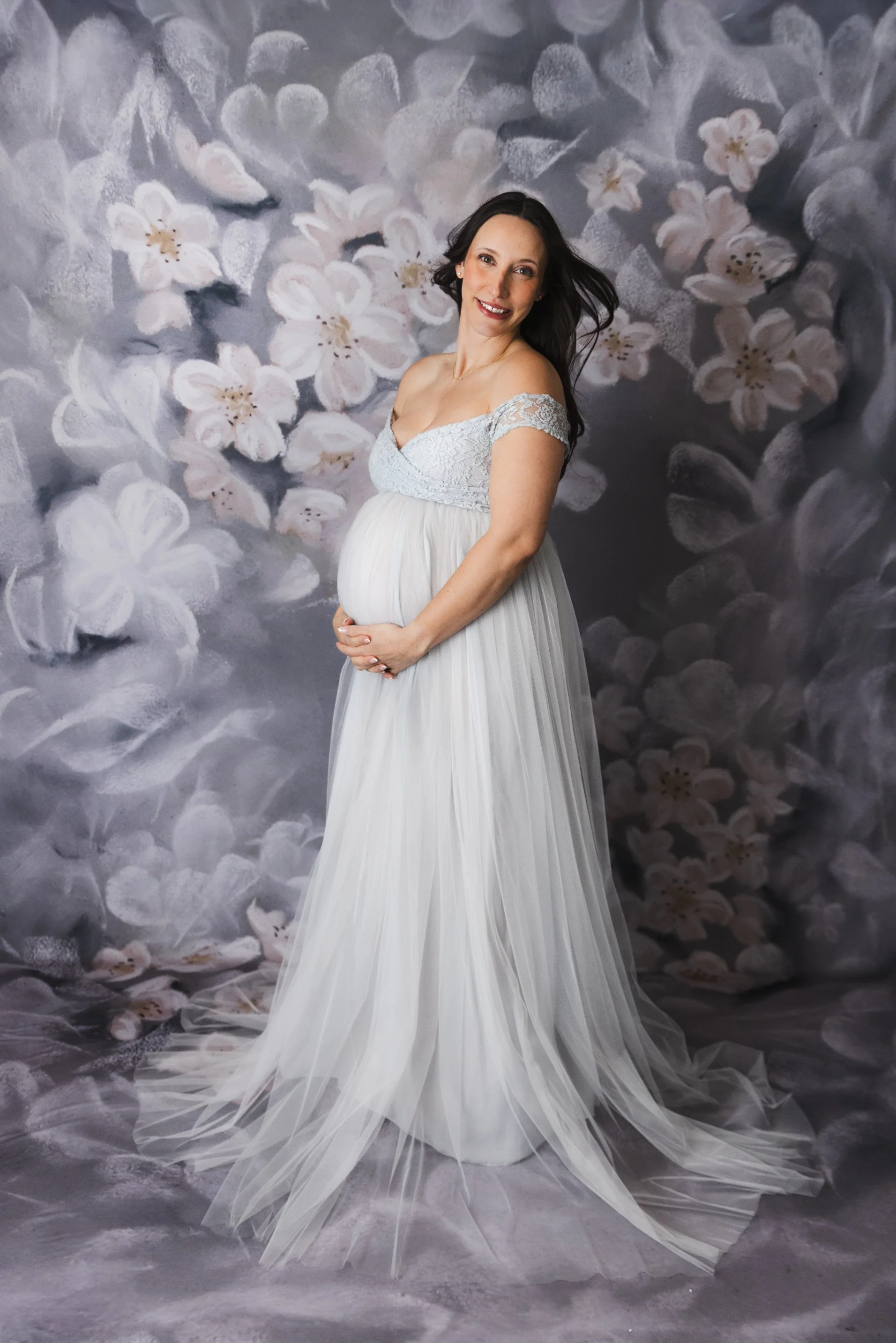 A pregnant woman wearing a silver tulle rental dress with off-the-shoulder embroidered corset, in a studio maternity photoshoot in Calgary