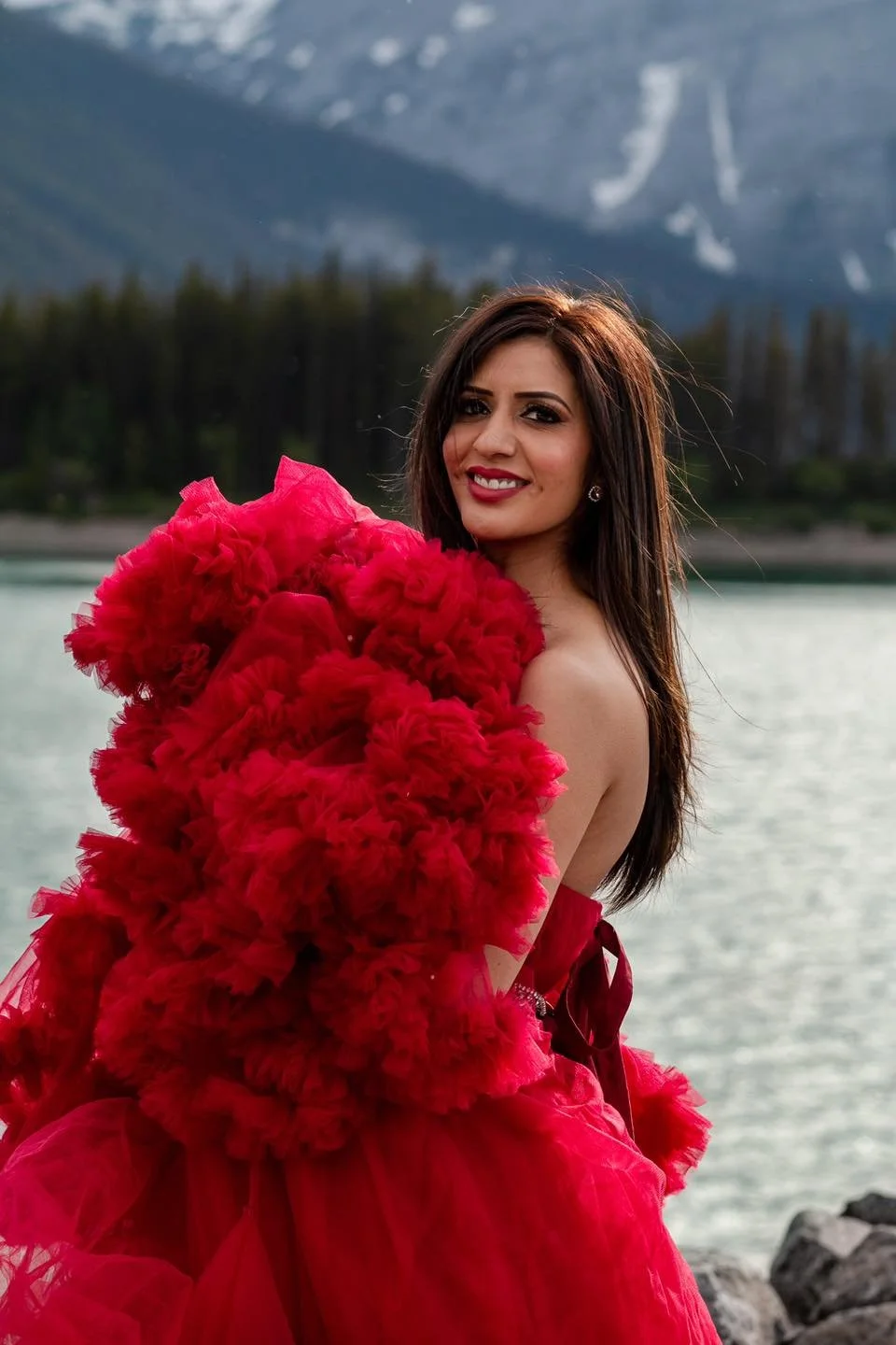 A woman wearing a red gown, standing in the mountains in an outdoor photoshoot in Calgary