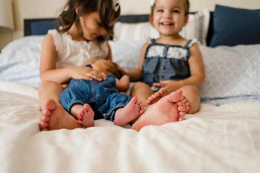 siblings on a bed, two toddlers and a newborn