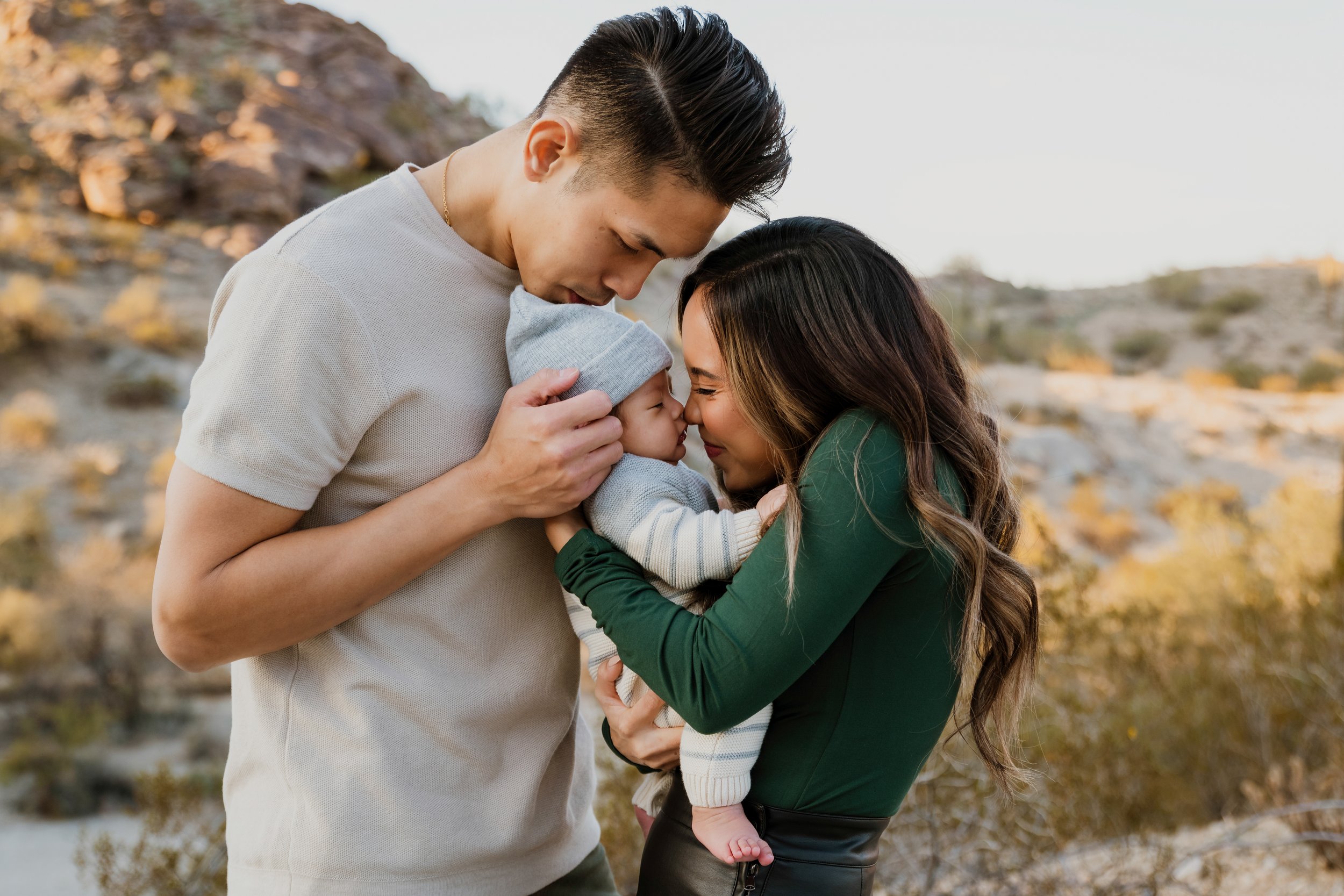 A couple embracing their baby in an outdoor setting with a rocky background.