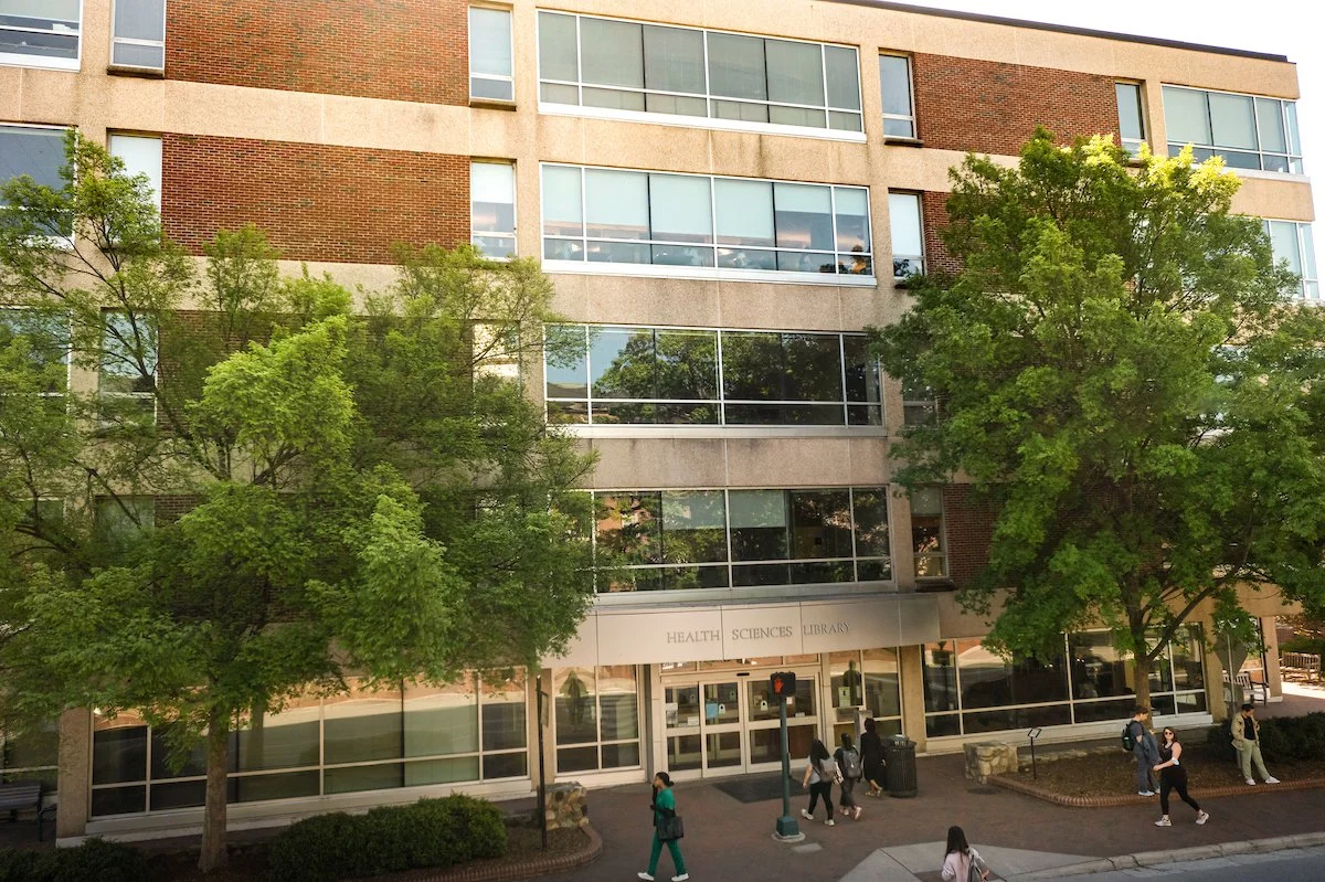 Front of Health Sciences Library building with green trees out front and people walking on the sidewalk