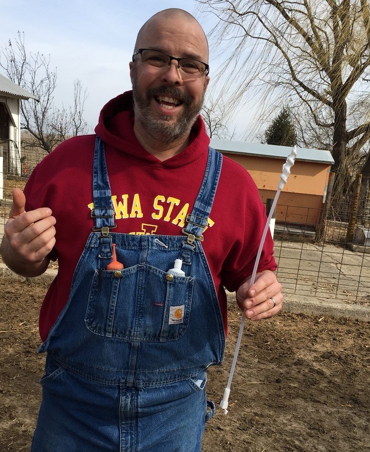 Garin wearing overalls and an ISU Cyclone sweatshirt. He is holding a flexible rod with a spiral end. This is a "straw" for artificially inseminated the pigs.