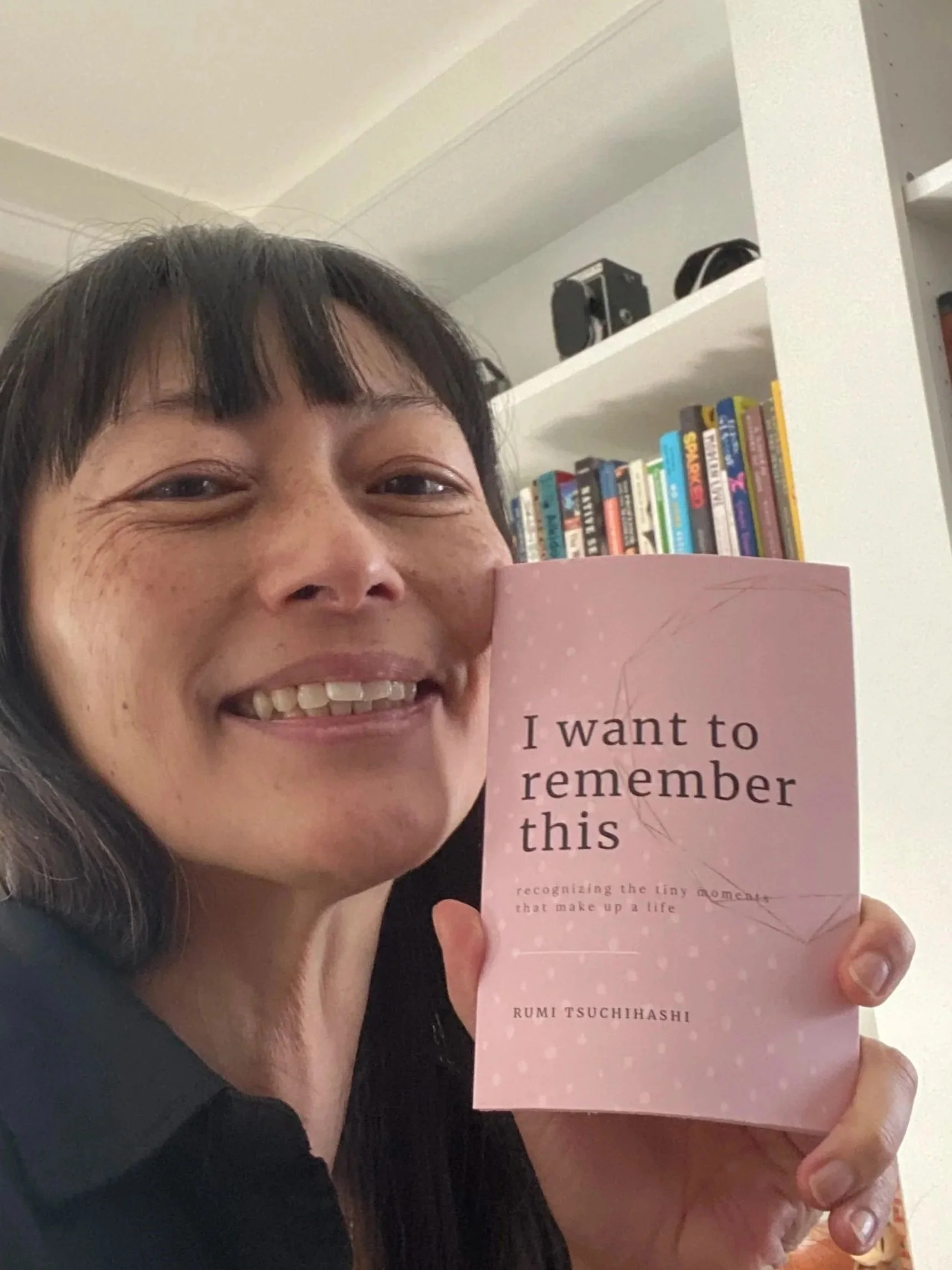Face of woman with black hair holding up a small pink book (Copy)