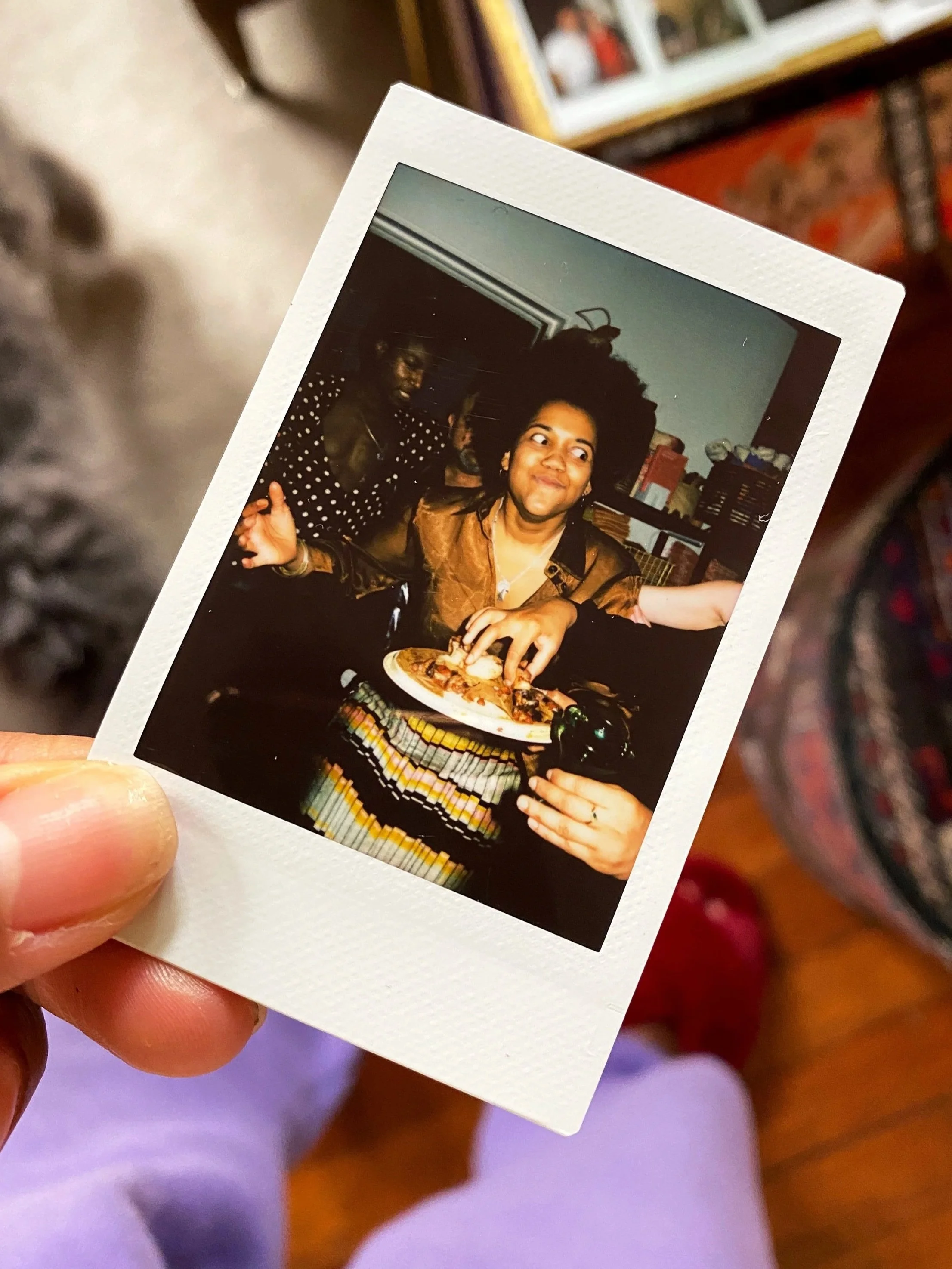 A woman sitting at a dining table with a plate of food, smiling, in a room with bookshelves.