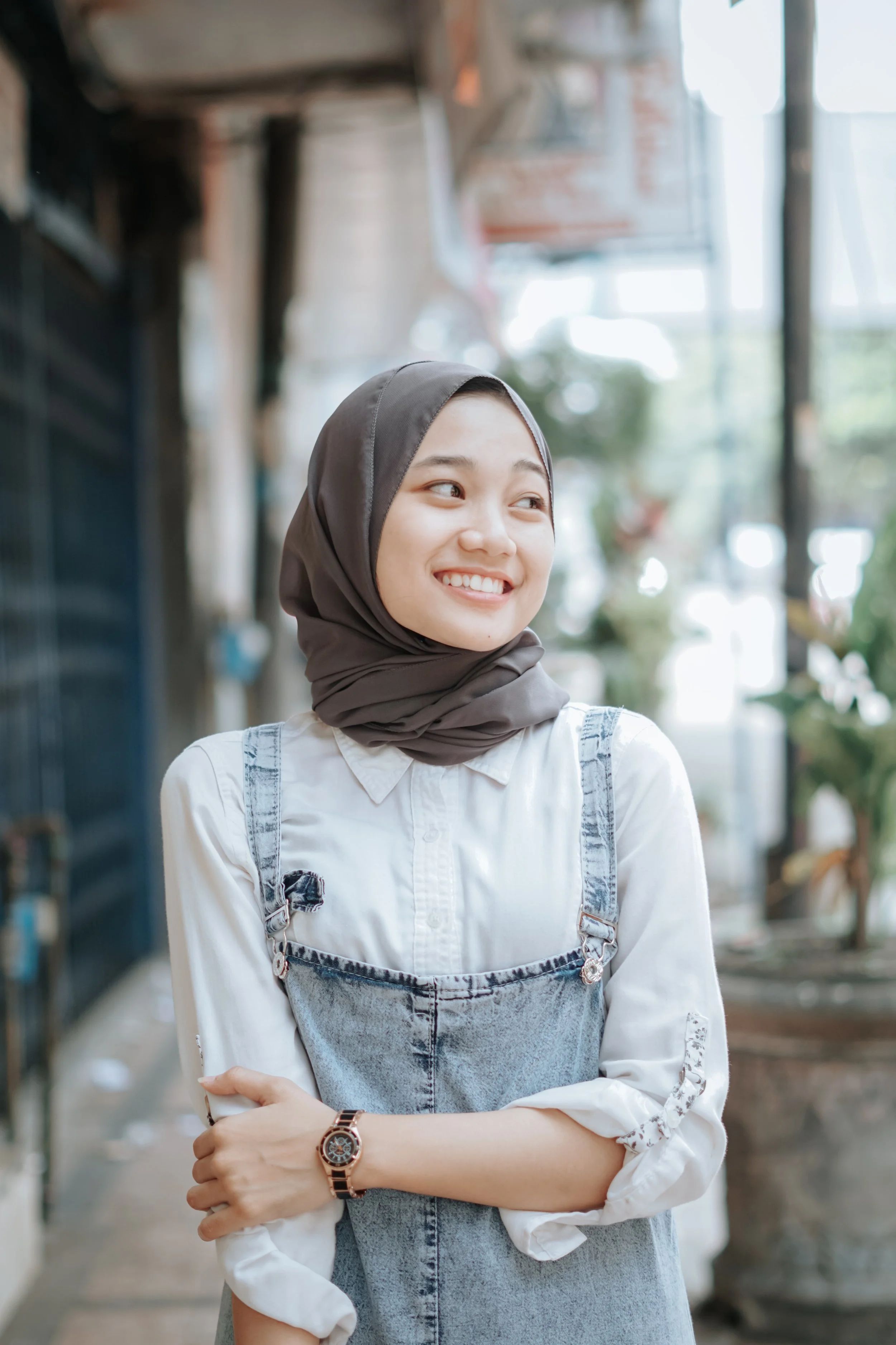 East-Asian woman in a hijab smiling, looking off to the side.