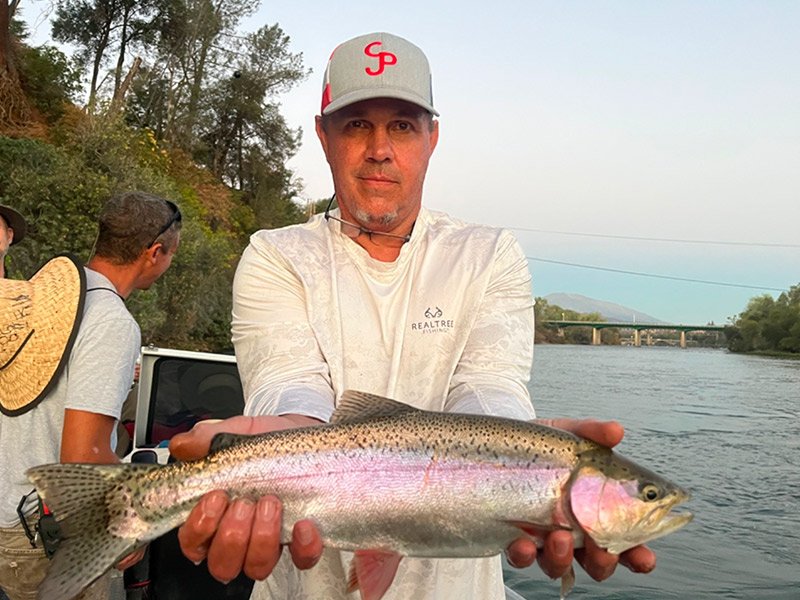 man holding large trout he caught on the sacramento river with a fishing expert in Redding, California