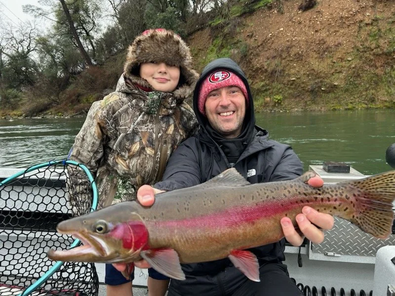 Father and son guided fishing trip on the Feather River in northern California holding a steelhead trout to show the camera