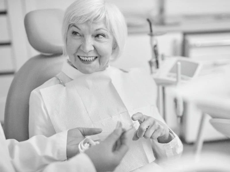 An old woman sitting in a dental chair gesturing towards dental implants