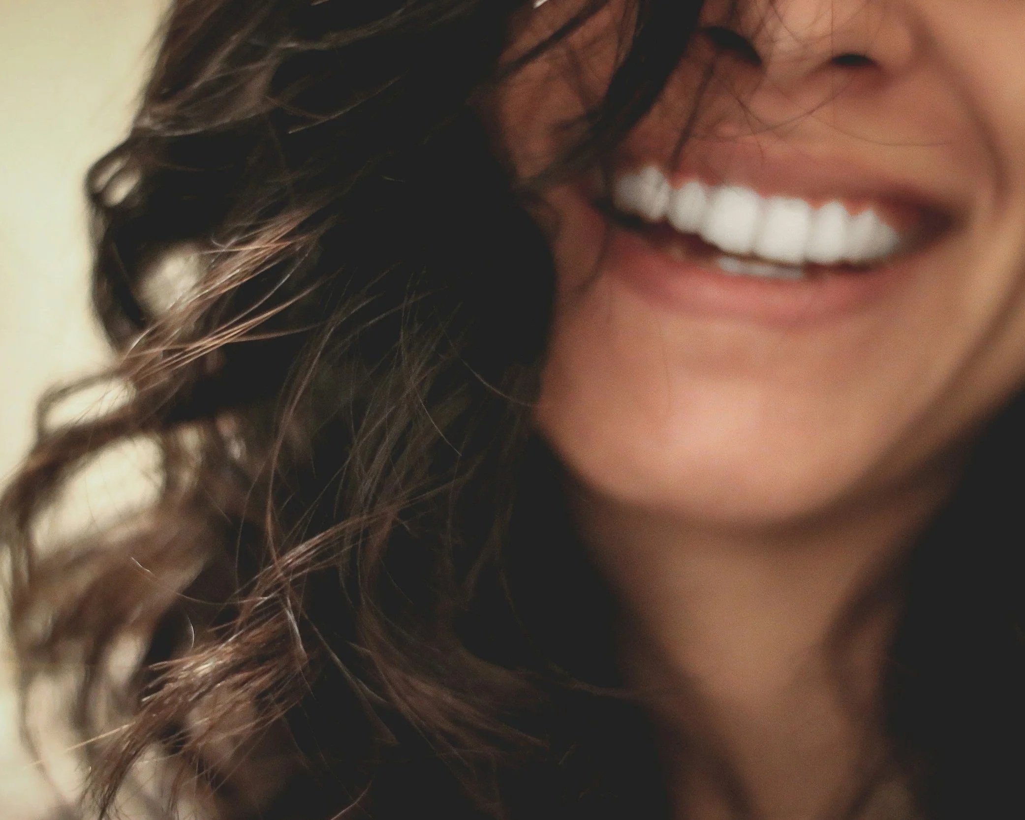 Close-up of a person's face showing a wide smile with white teeth, a nose, and long wavy hair.