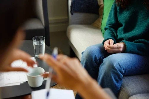 To personer sidder i en stue, en person tager notater, mens den anden person sidder på en sofa.