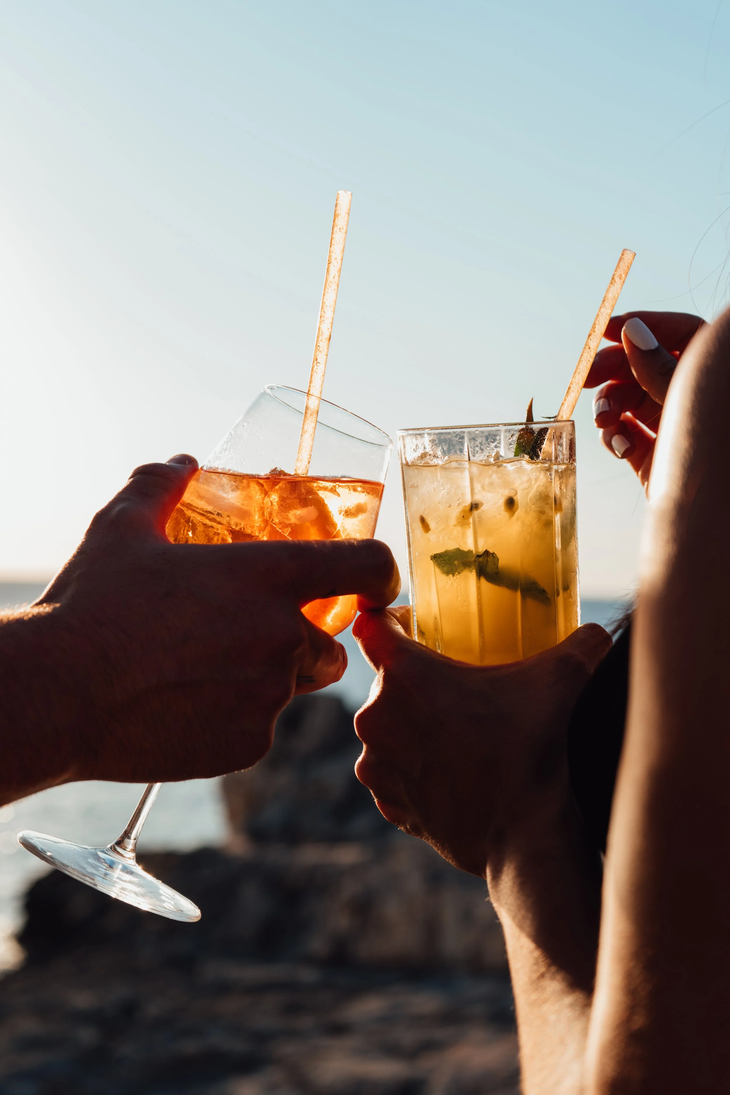 Personas levantando copas de cócteles en una reunión al aire libre con el mar de fondo, disfrutando de una bebida refrescante durante el atardecer.