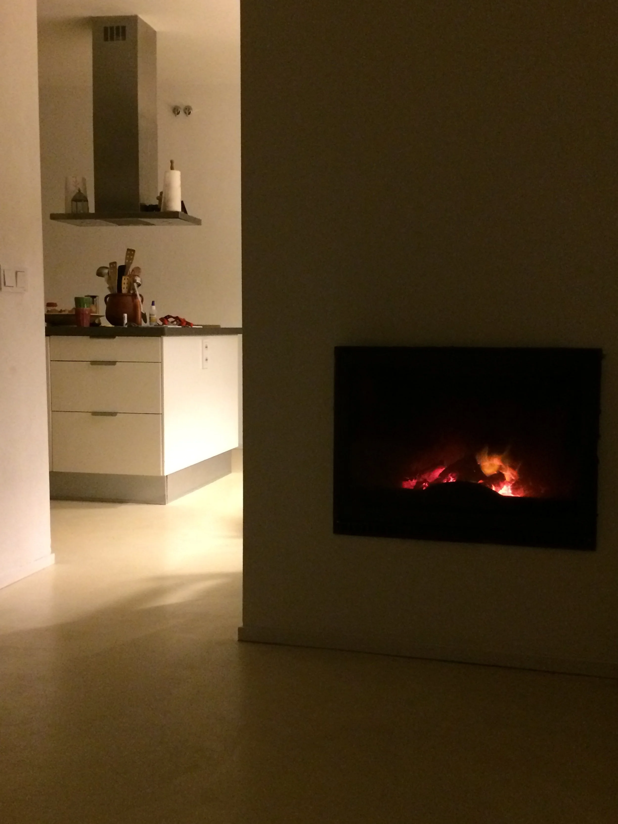 Dimly lit room with a modern kitchen on the left and a fireplace on the right, casting a warm glow.