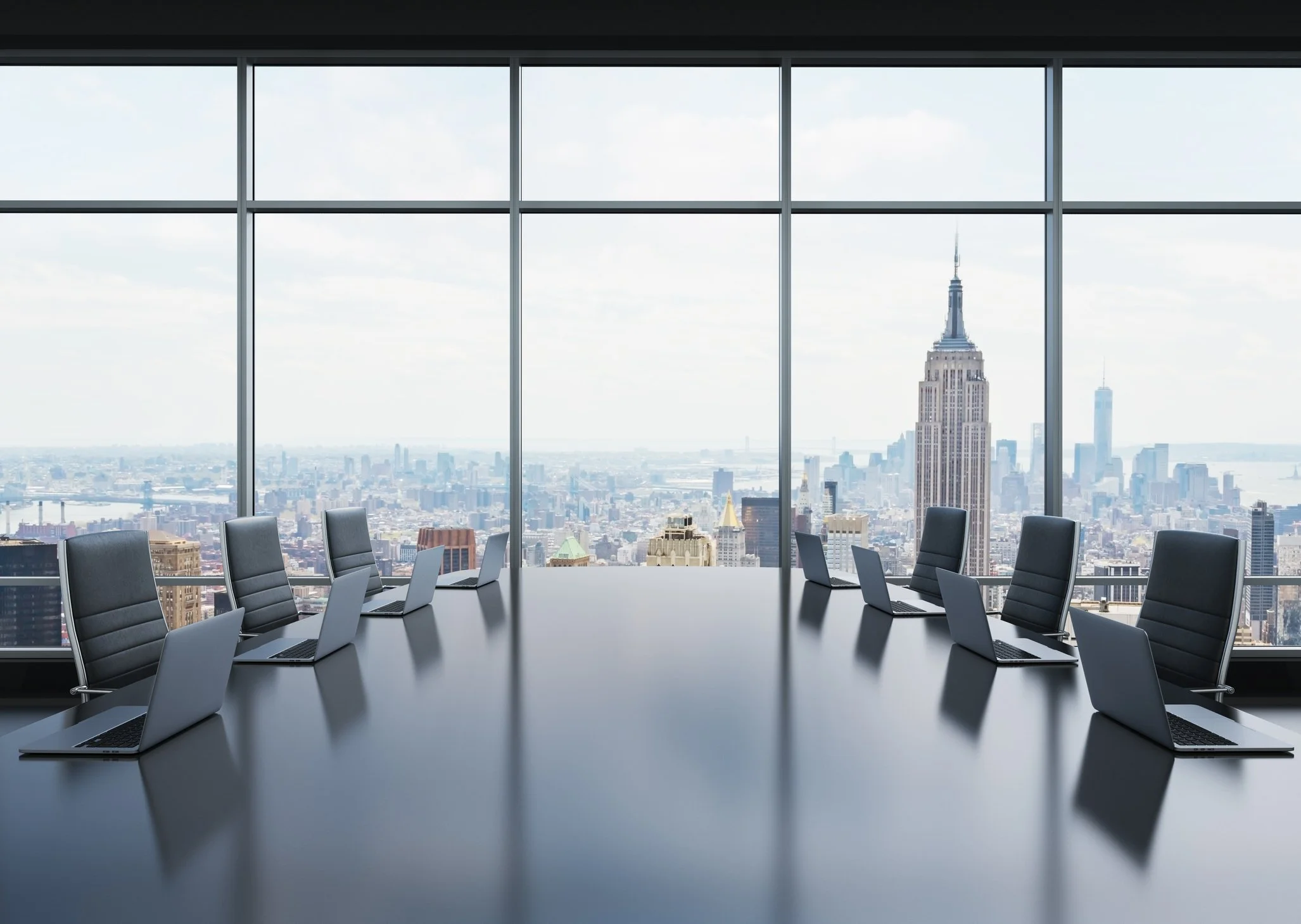 Modern conference room with black chairs and open laptops, overlooking New York City skyline through large glass windows.