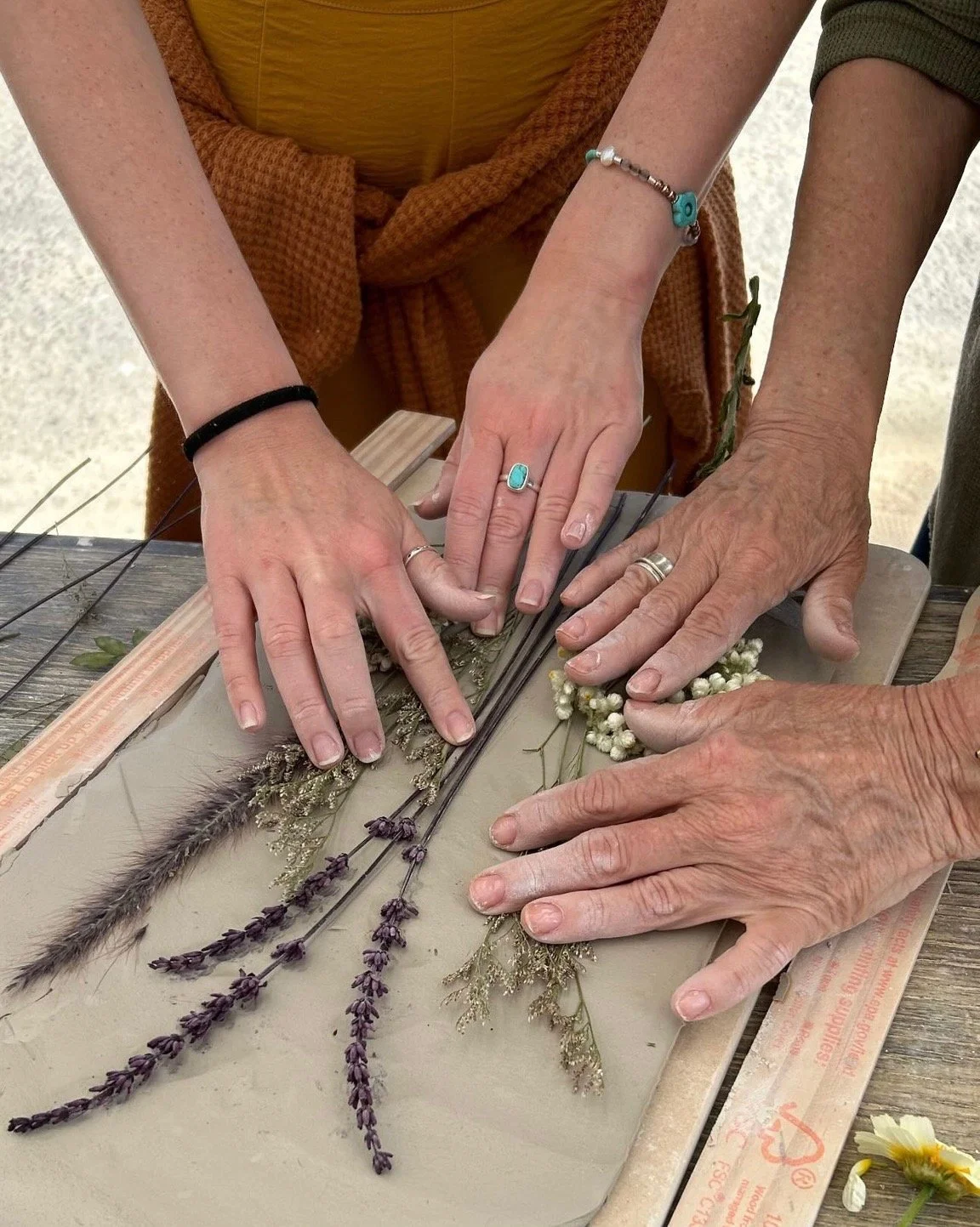 Family working together pressing dried flowers into clay at The Mudd House's Mother's Day Petals & Platters workshop