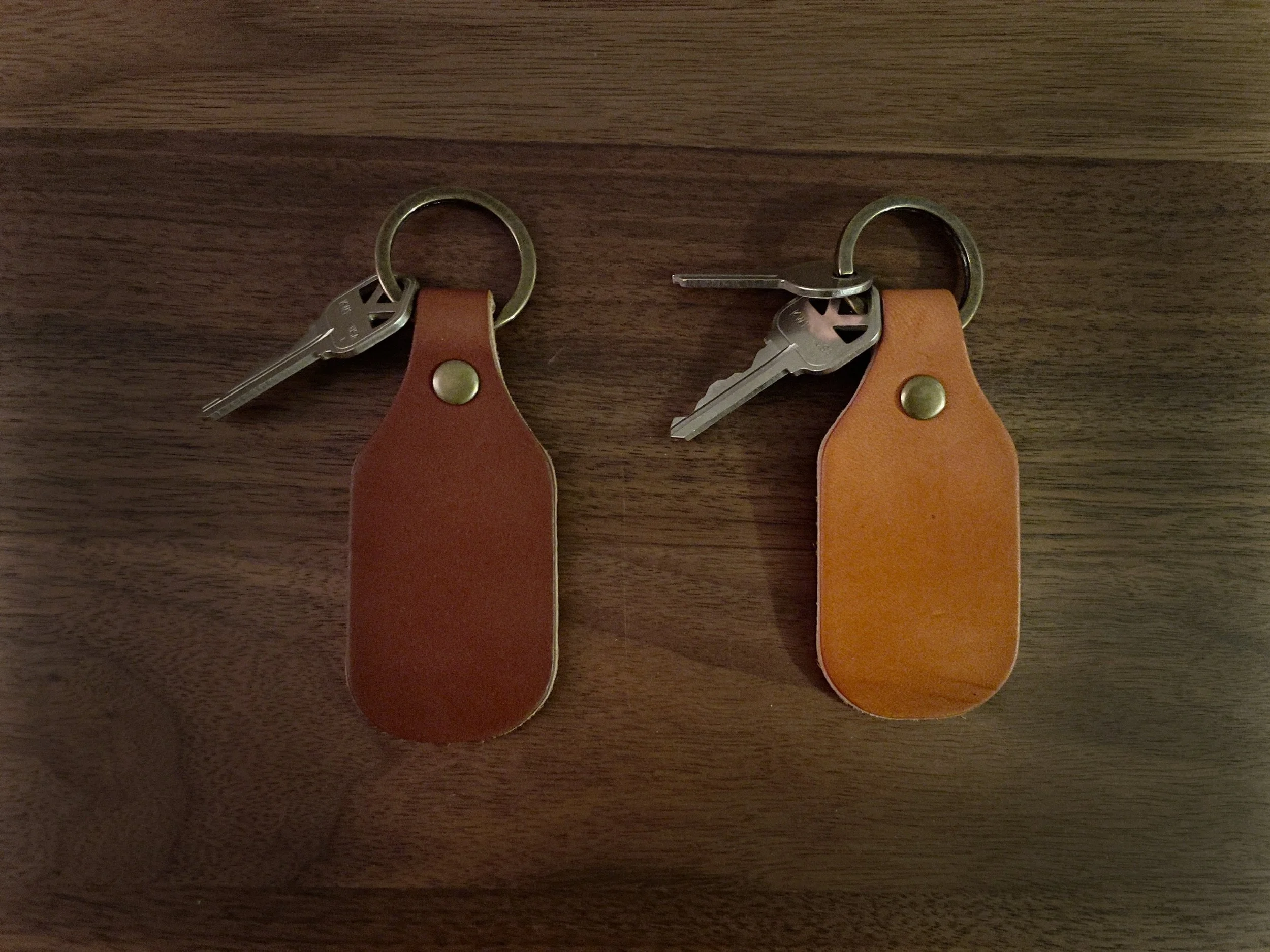 Two sets of keys with leather keychains on a wooden surface.