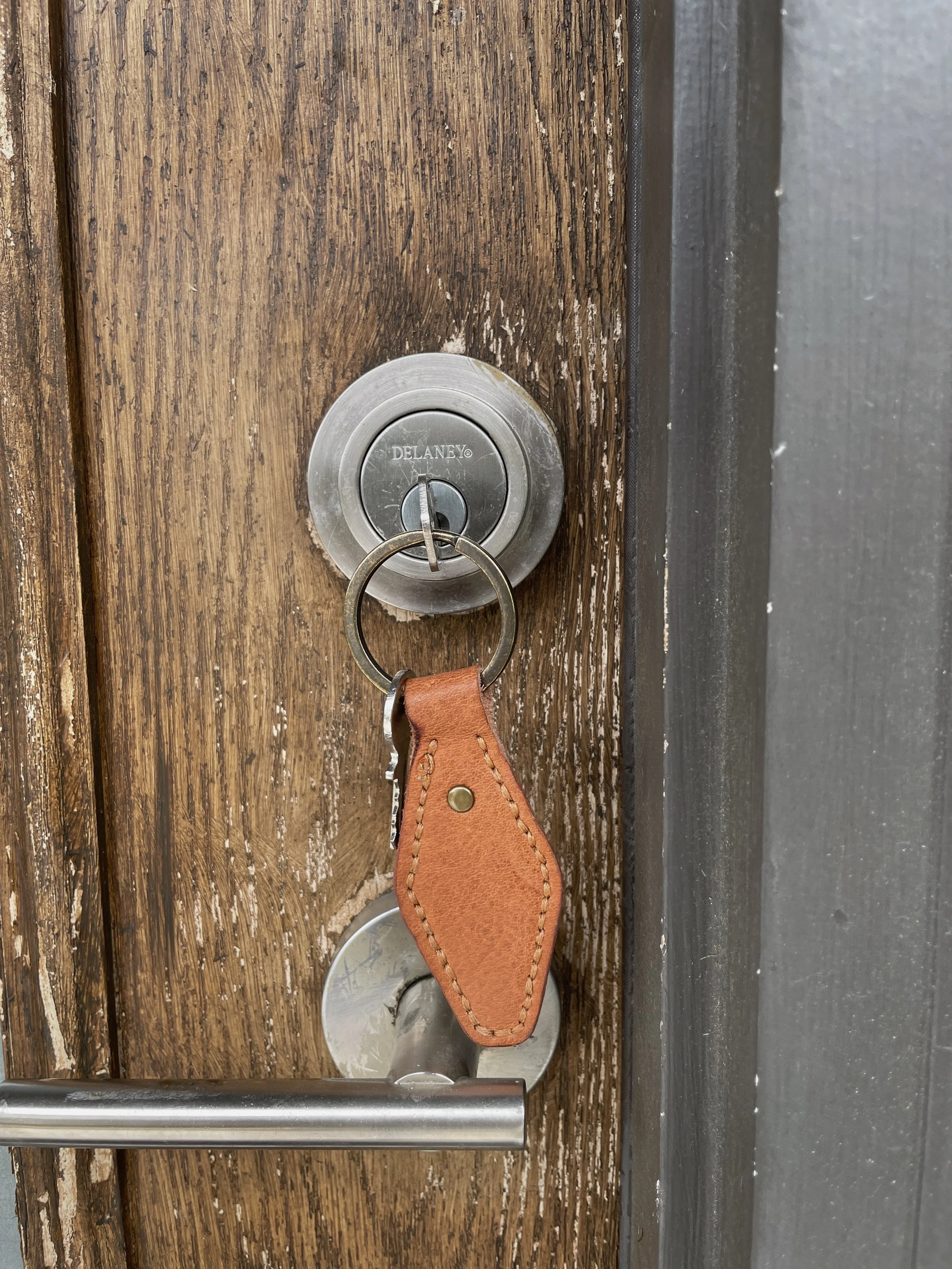 Close-up of a silver door lock with a keyring holding a leather key fob on a wooden door.