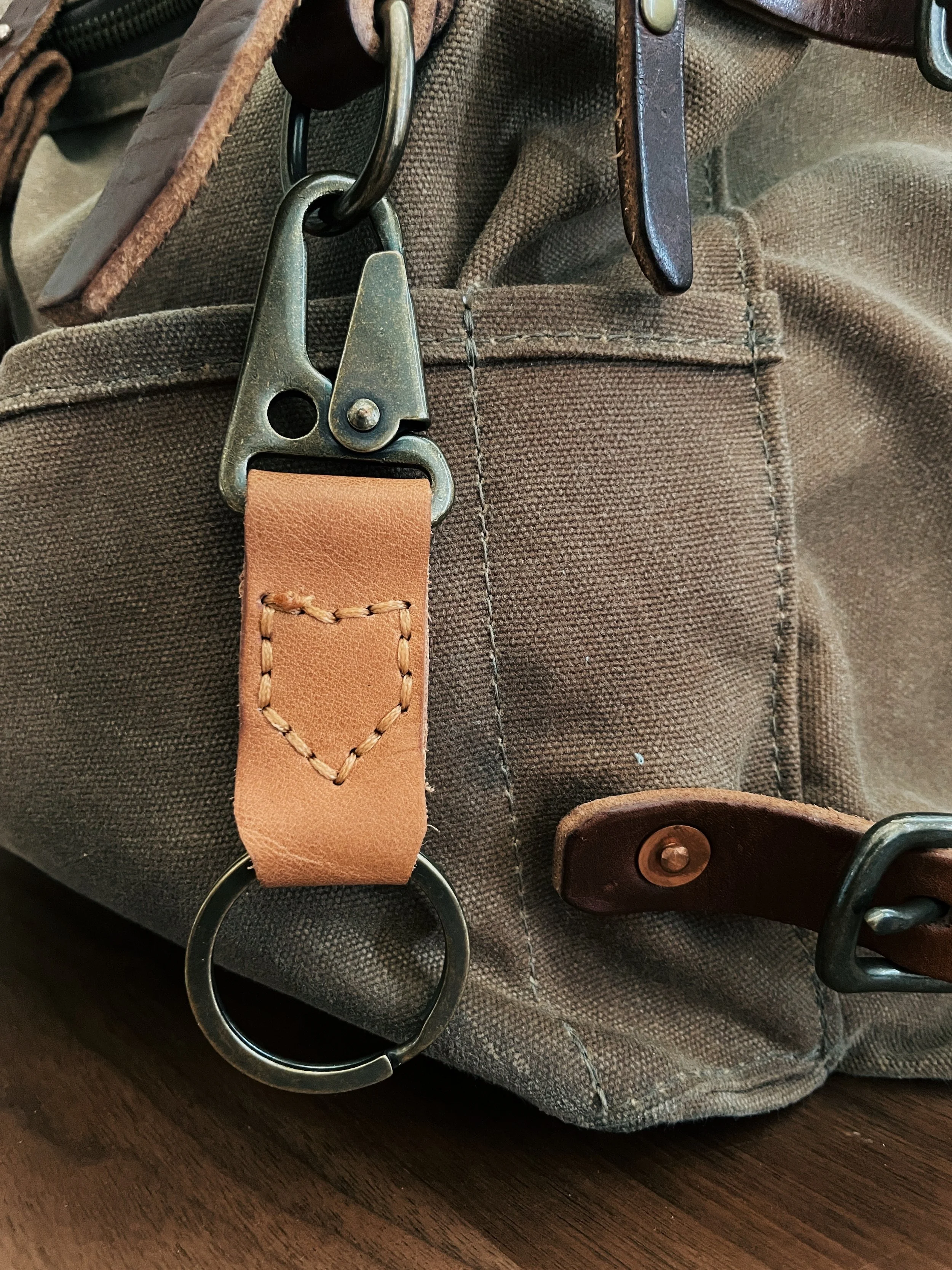 Close-up of a brown canvas bag with leather strap and metal hardware, including a keyring and clip.