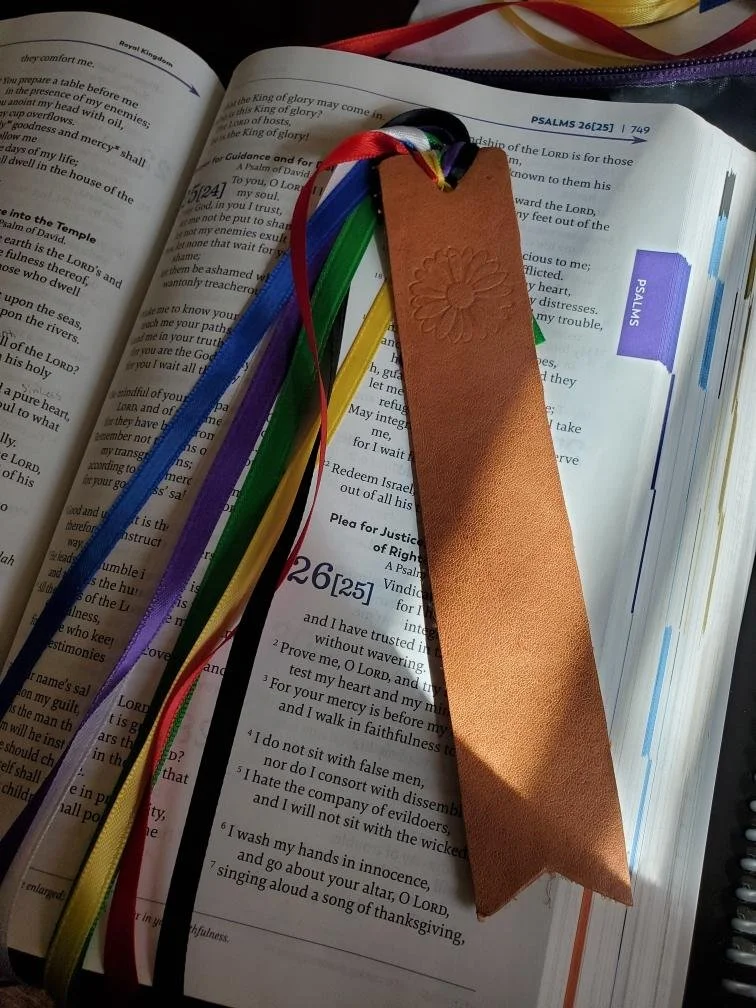 Open Bible with colorful ribbons and a brown leather bookmark resting on the page.