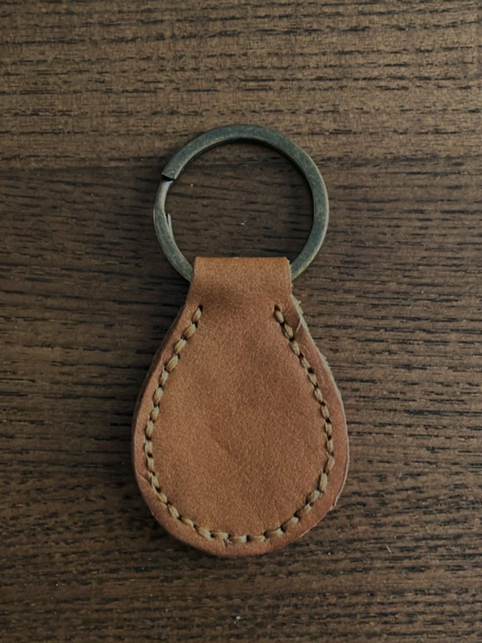 Leather keychain with metal keyring on wooden surface.