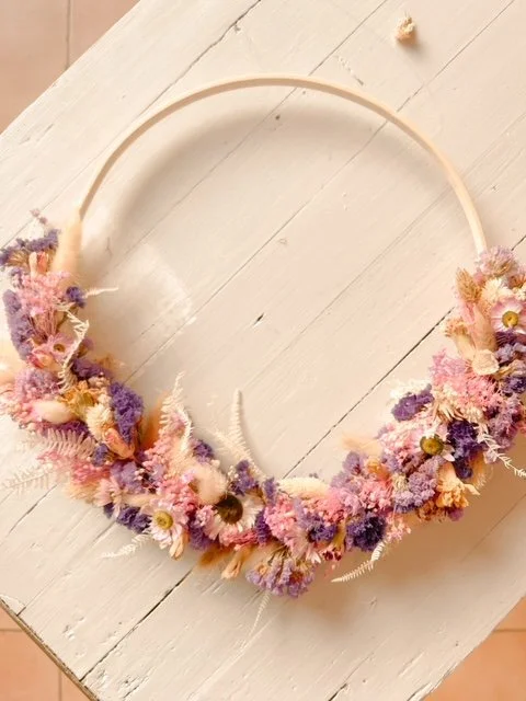 Blumenkranz mit bunten Trockenblumen in Rosa, Lila und Cremefarben auf weißem Holztisch