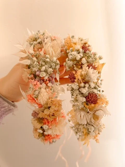 Eine Hand hält einen geflochtenen Kranz aus getrockneten Blumen in Pastellfarben.