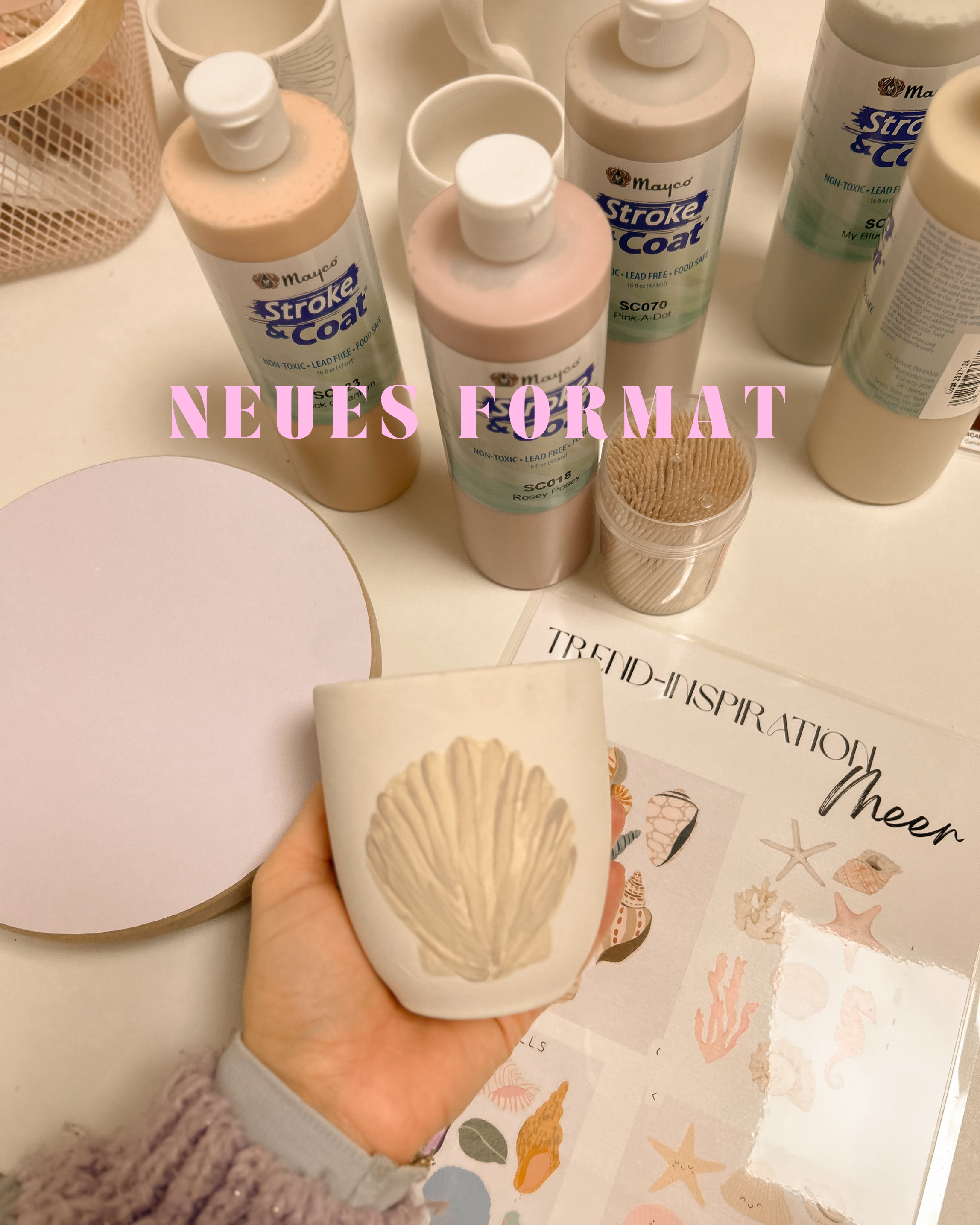 Kunsthandwerk mit Muschelmuster, Wasserflaschen mit Beschriftungen, Becher, Pinsel, und Dekorationen im Meeresstil, Text 'Neues Format' in Lila
