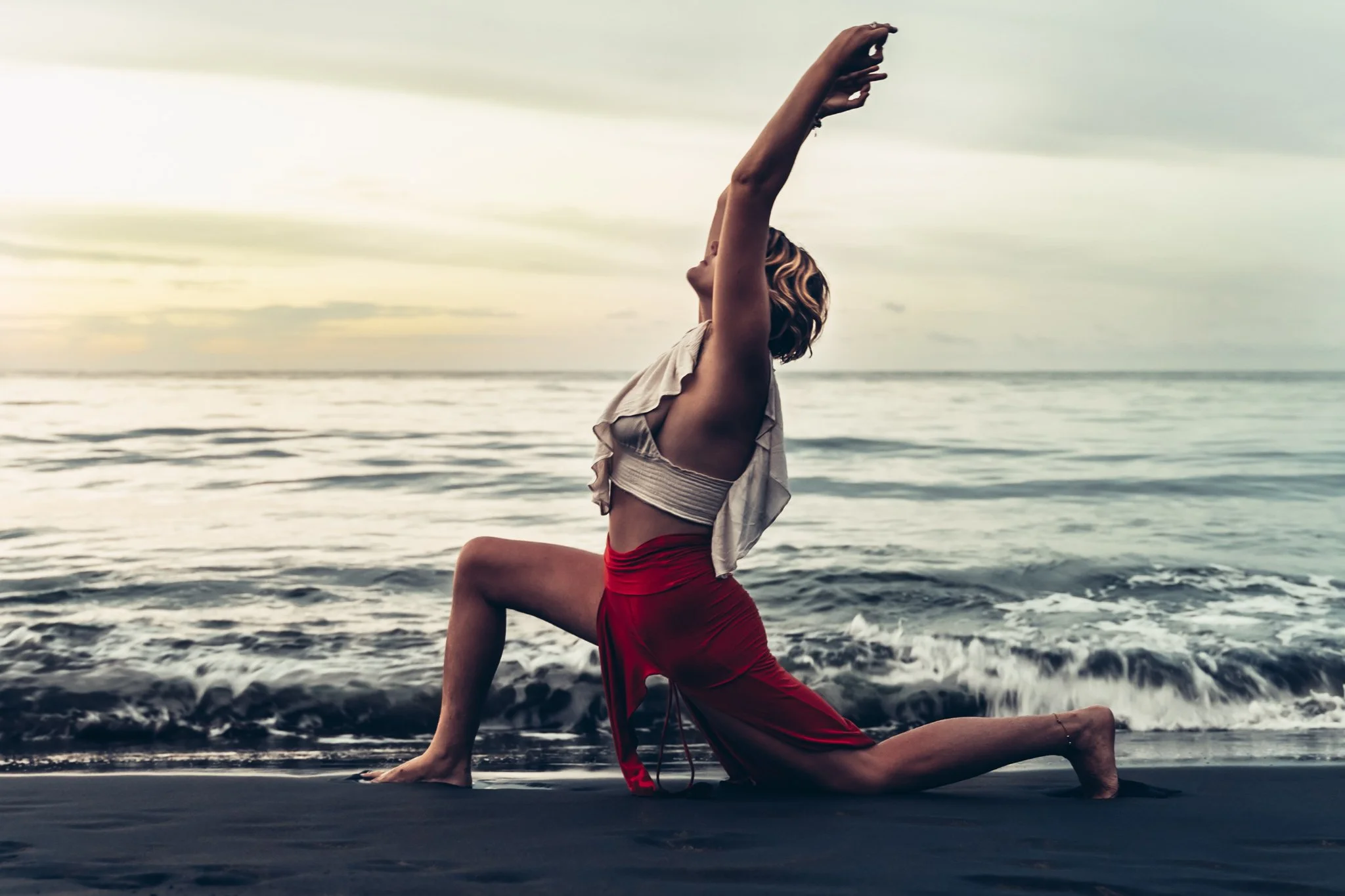 Woman in yoga pose on a beach with ocean waves in the background