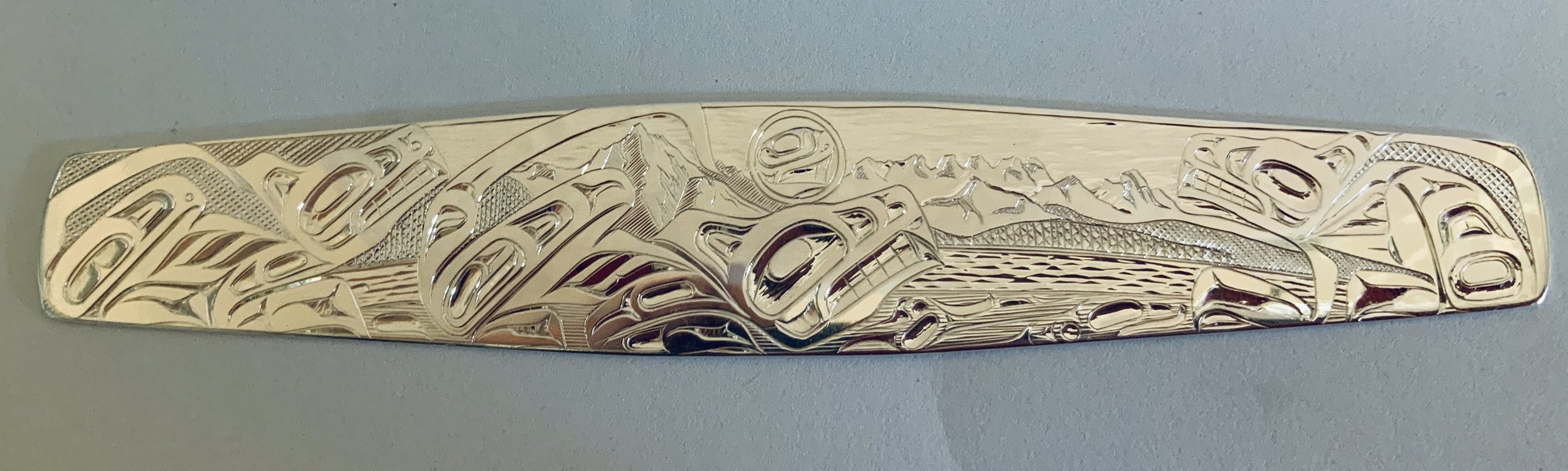 A carved silver bracelet by special order, featuring a wolf design and mountain scenery *not available*