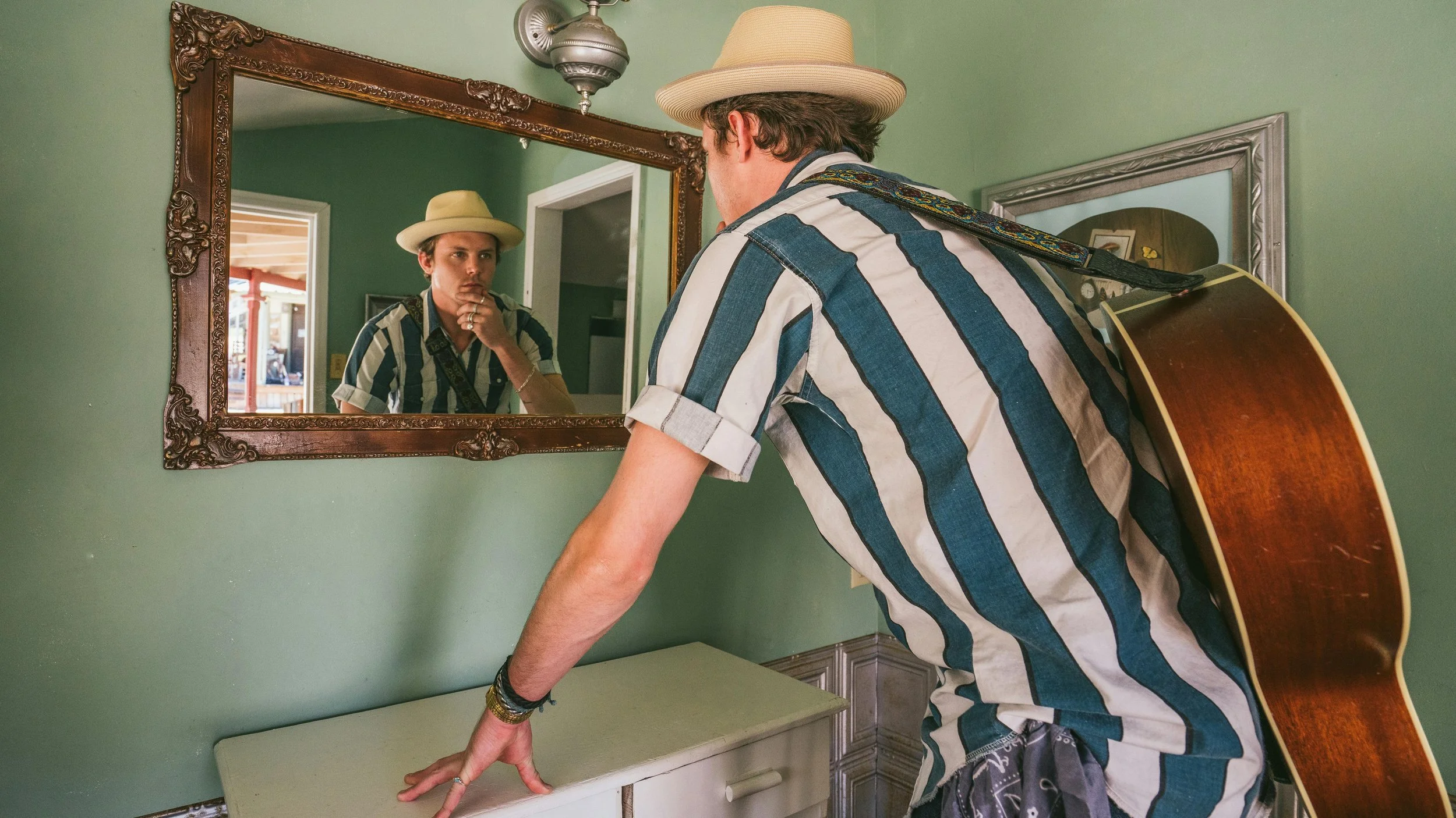 A man with a guitar slung over his shoulder looks in the mirror to check his appearance with a look of curiosity. Dr. Waldron gives an overview of signs that EMDR therapy is working for her clients in San Francisco and Corte Madera (Marin) California