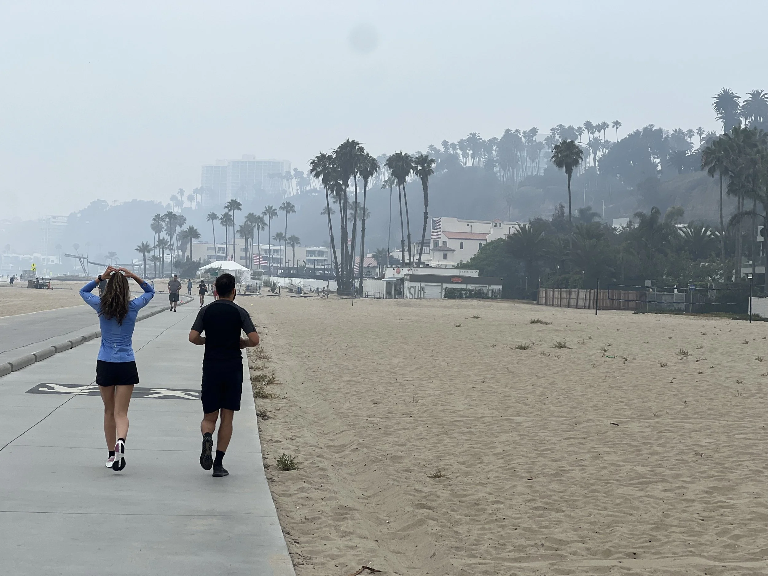 A couple walk and jog together on the beach in Santa Monica, California. Dr. Amy Waldron provides EMDR therapy via telehealth for clients all over California.
