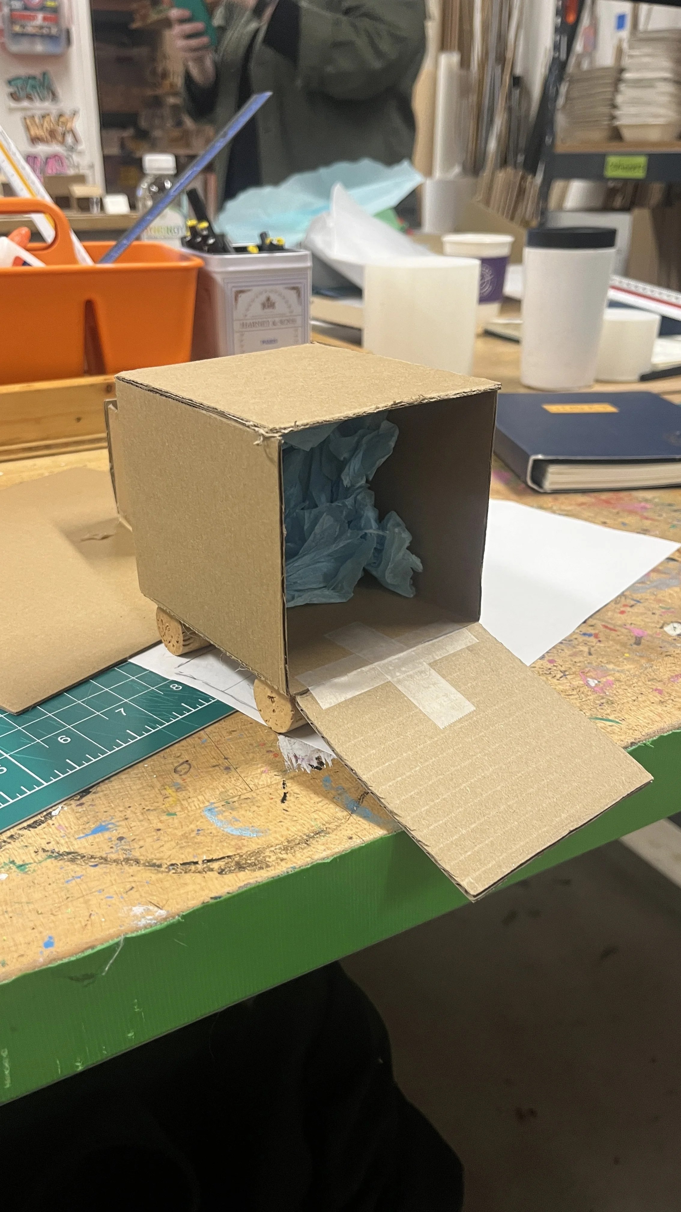 Cardboard model with cork wheels and blue tissue paper for padding inside