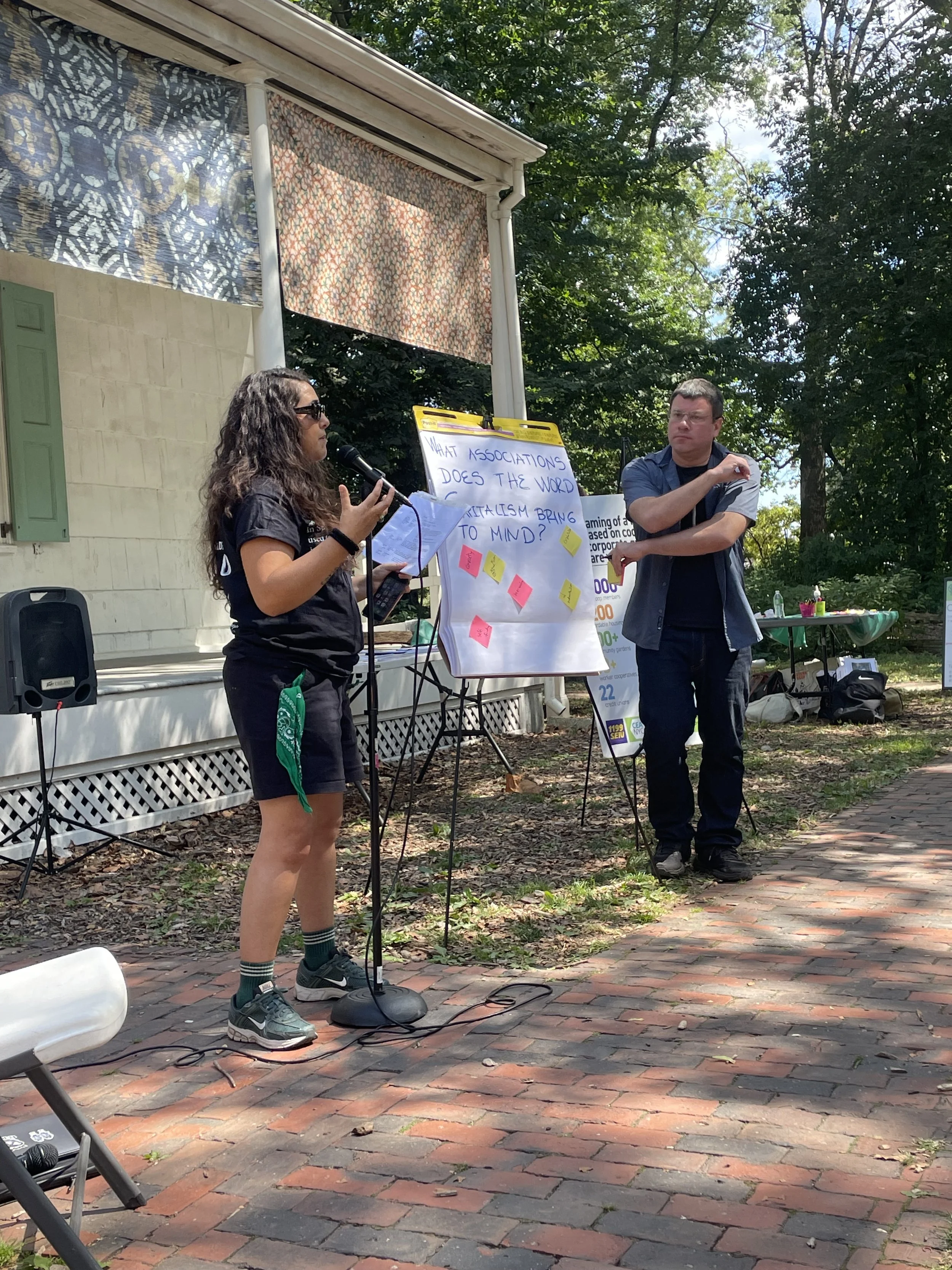 Woman stands in front of poster with sticky notes reading "what does the word capitalism bring to mind?"