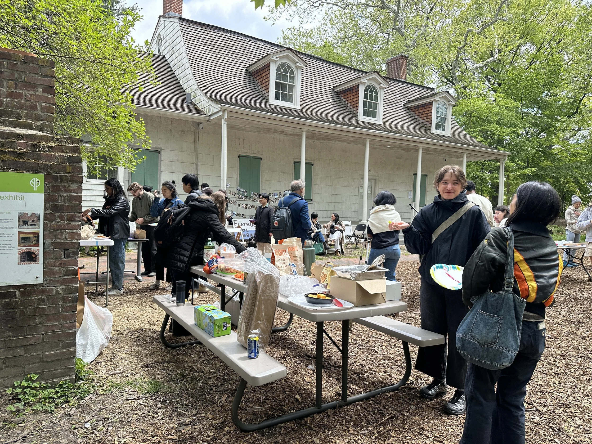 People gather around picnic tables in front of the lefferts house