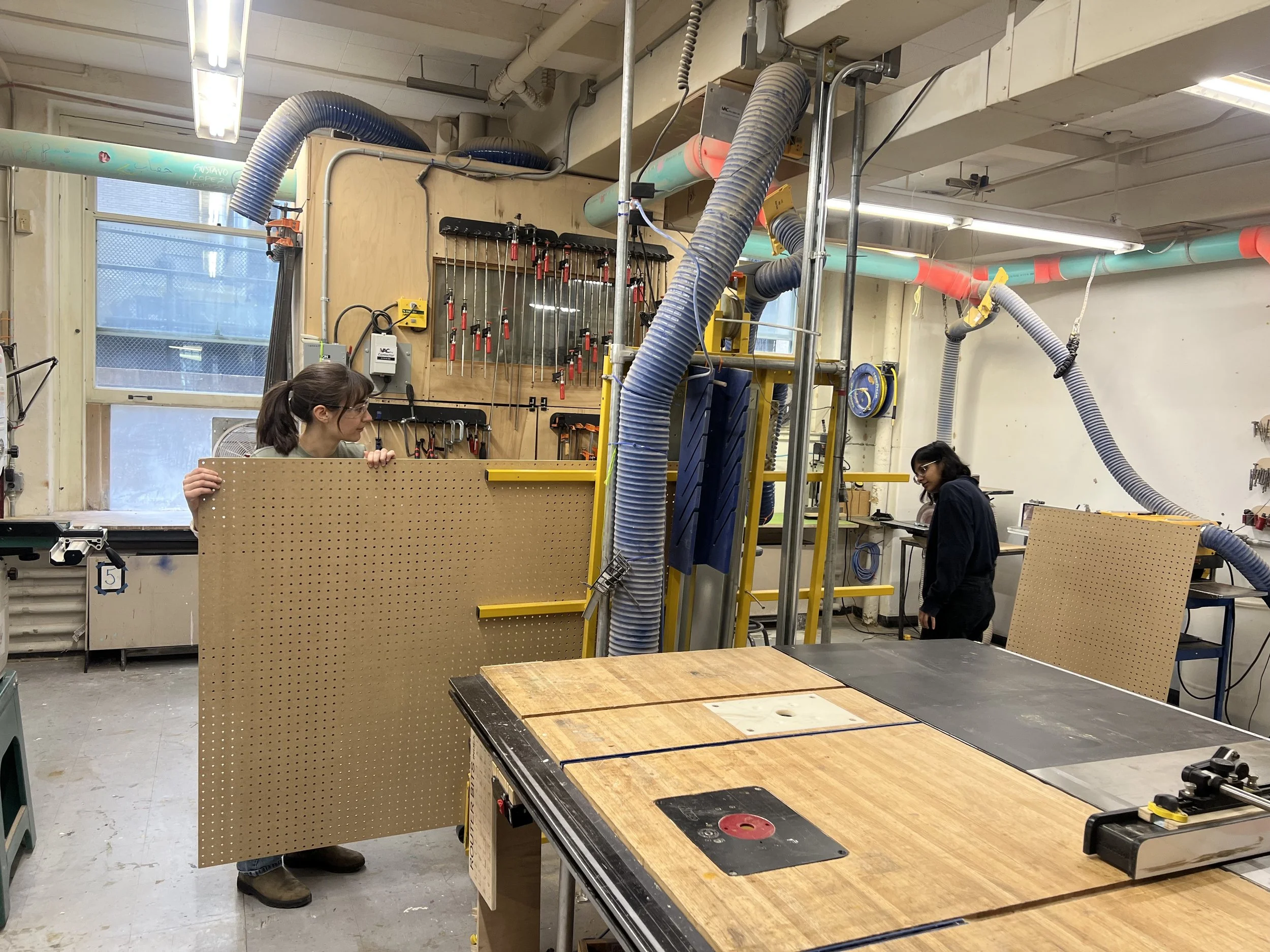 Young woman guides pagboard through a vertical saw in a woodshop