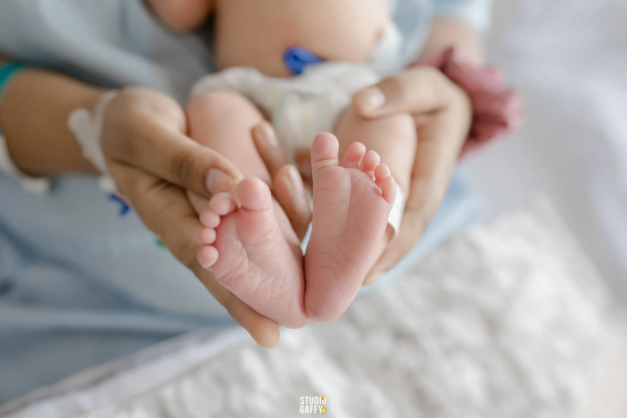 A close-up of a person's hands holding a tiny baby's feet, with the baby's body partially visible in the background.