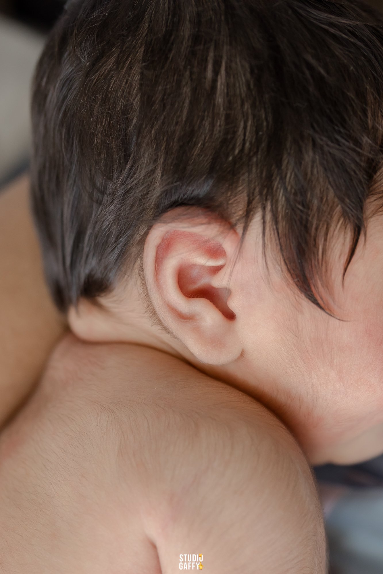 Close-up of a person's ear and short brown hair, showing the side of their head and neck.