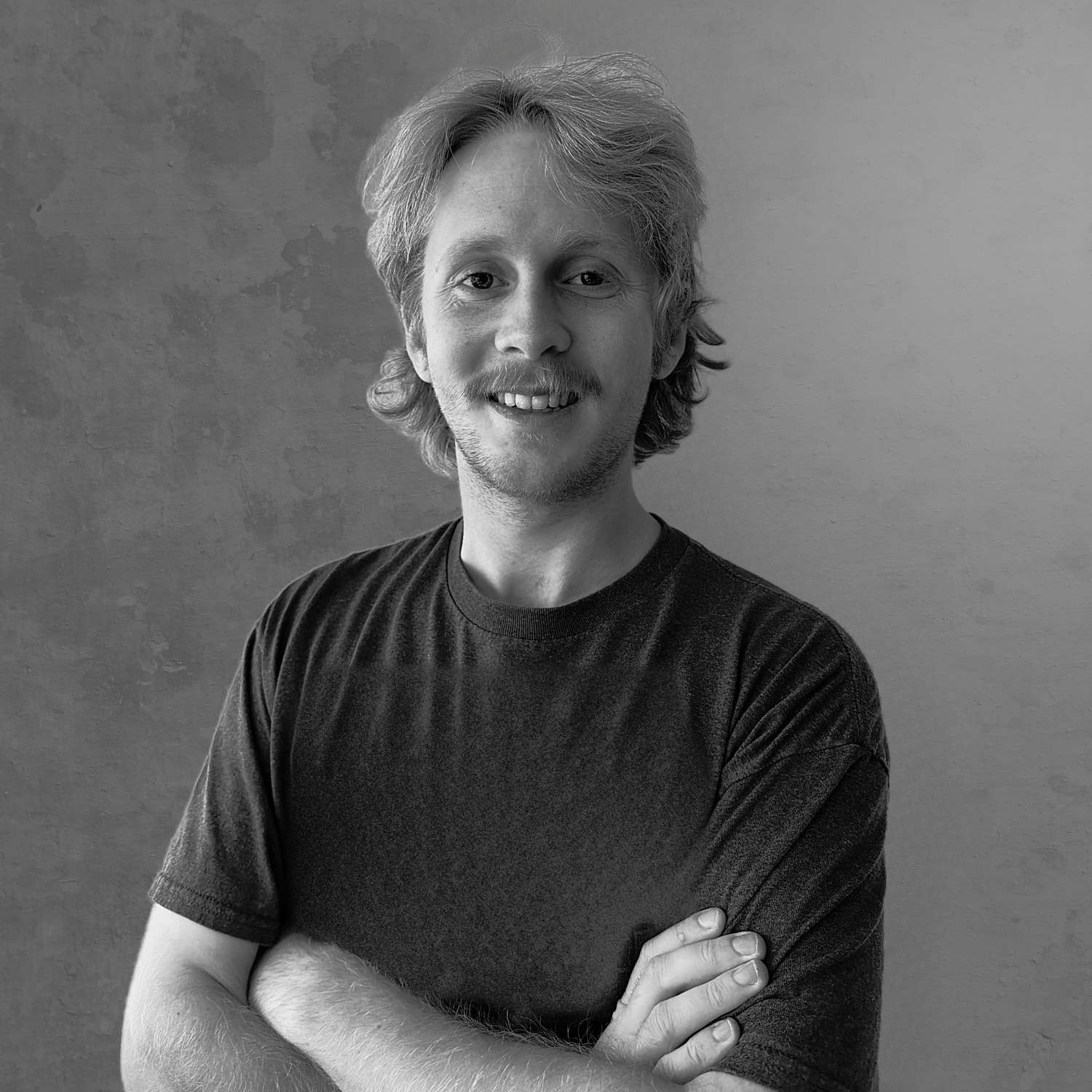 Black and white portrait of a smiling person against a textured wall background.