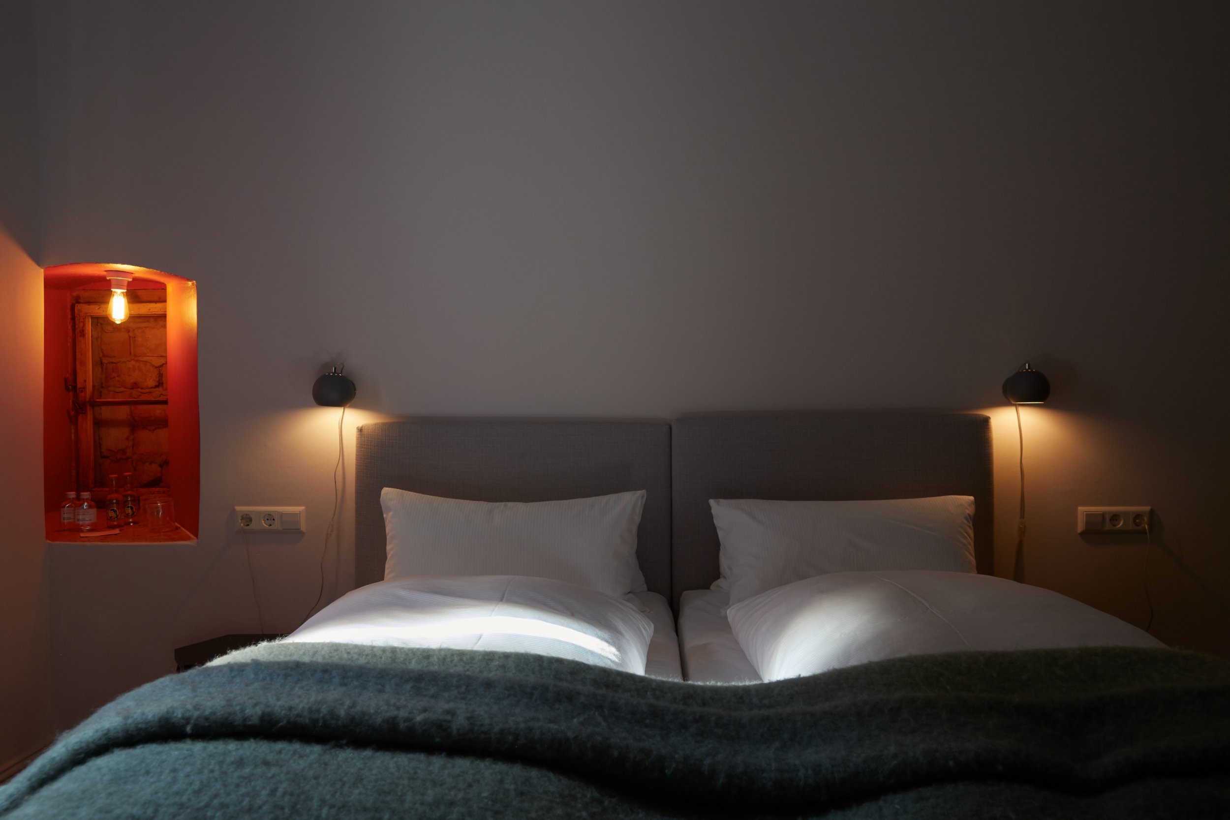 Hotel room with a bed, two pillows, bedside lamps, and a window with a painted frame
