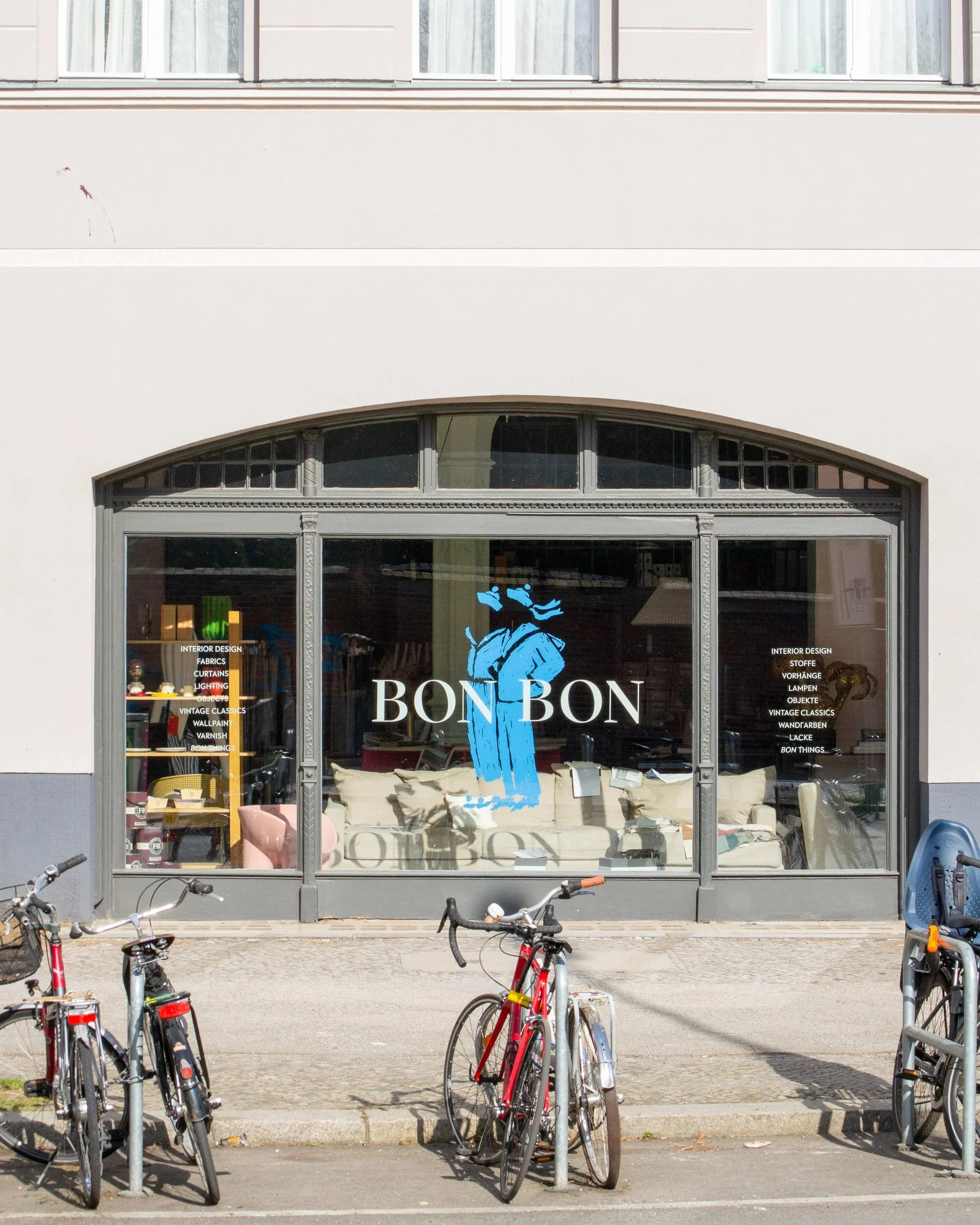 Storefront with large glass window displaying the name Bon Bon, with bicycles parked in front and a sofa visible inside.