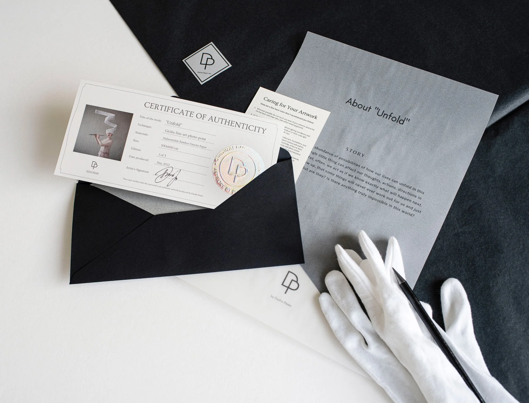 Black envelope, white gloves and letters of authenticity of psychorealism artist Dasha Pears artworks over a half white half black fabrics.