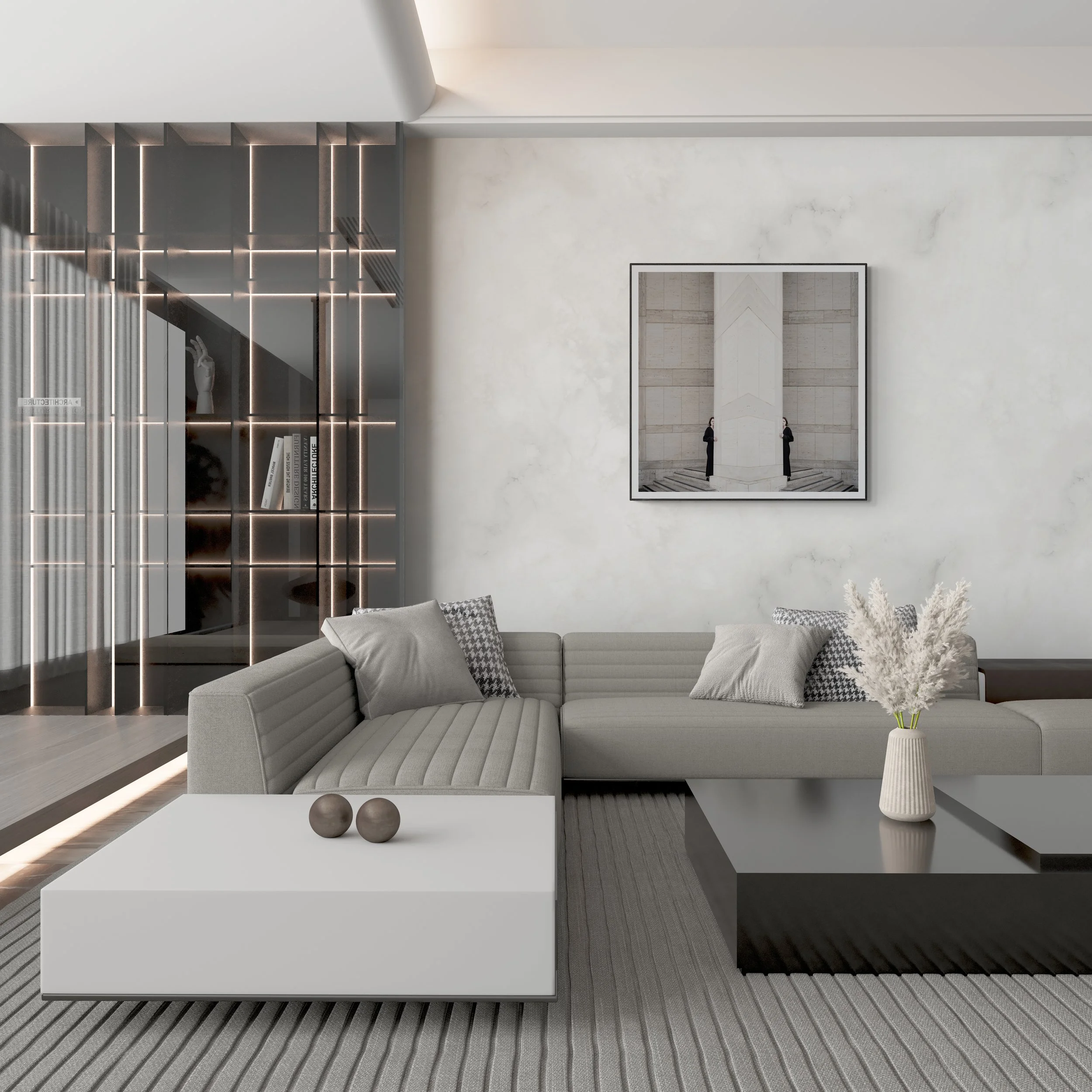 Modern living room with a light gray sectional sofa with patterned cushions, a black and white framed artwork on the white wall, a small white side table with a vase and plants, a textured gray area rug, a large mirror, and a sleek black and wood shelving unit with books and decorative items. The space features neutral tones and contemporary design elements.